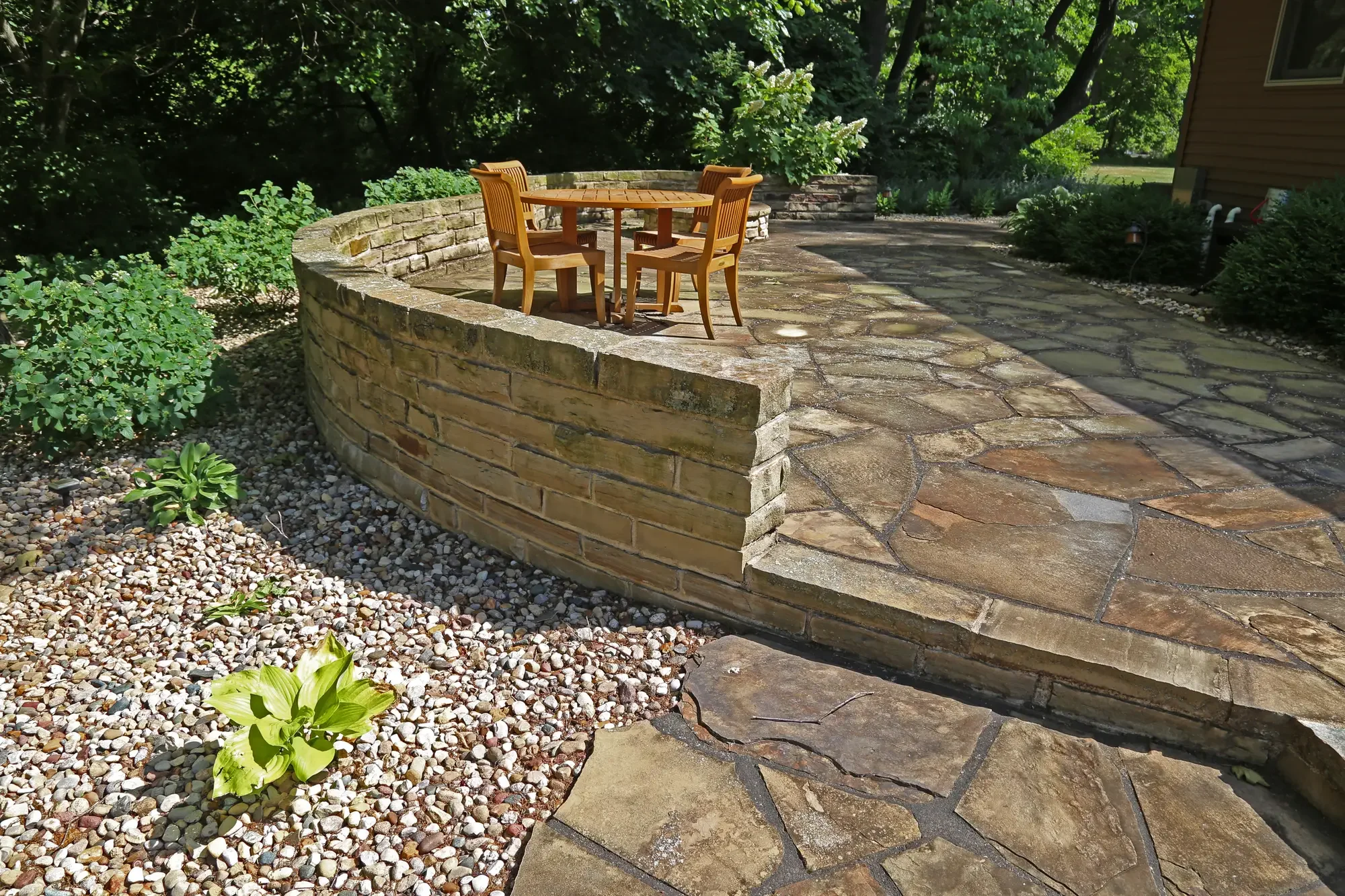 Curved natural stone retaining wall with flagstone patio and outdoor dining set by Green View in Central Illinois