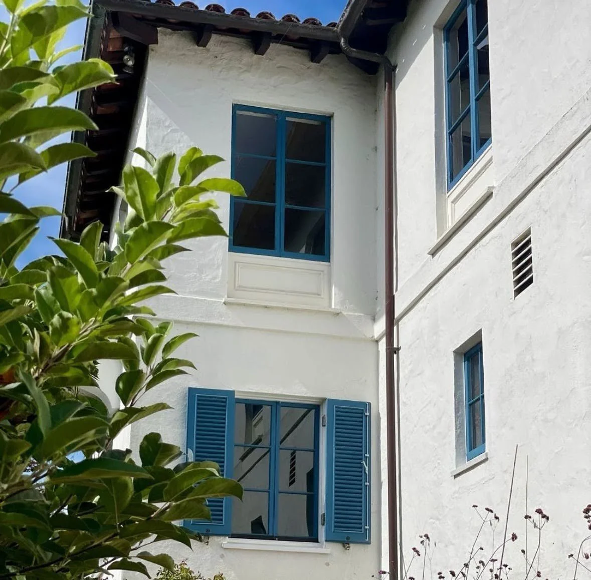Historic Spanish Mediterranean home in the Bay Area with white stucco, blue casement windows, louvered shutters and clay tile roof
