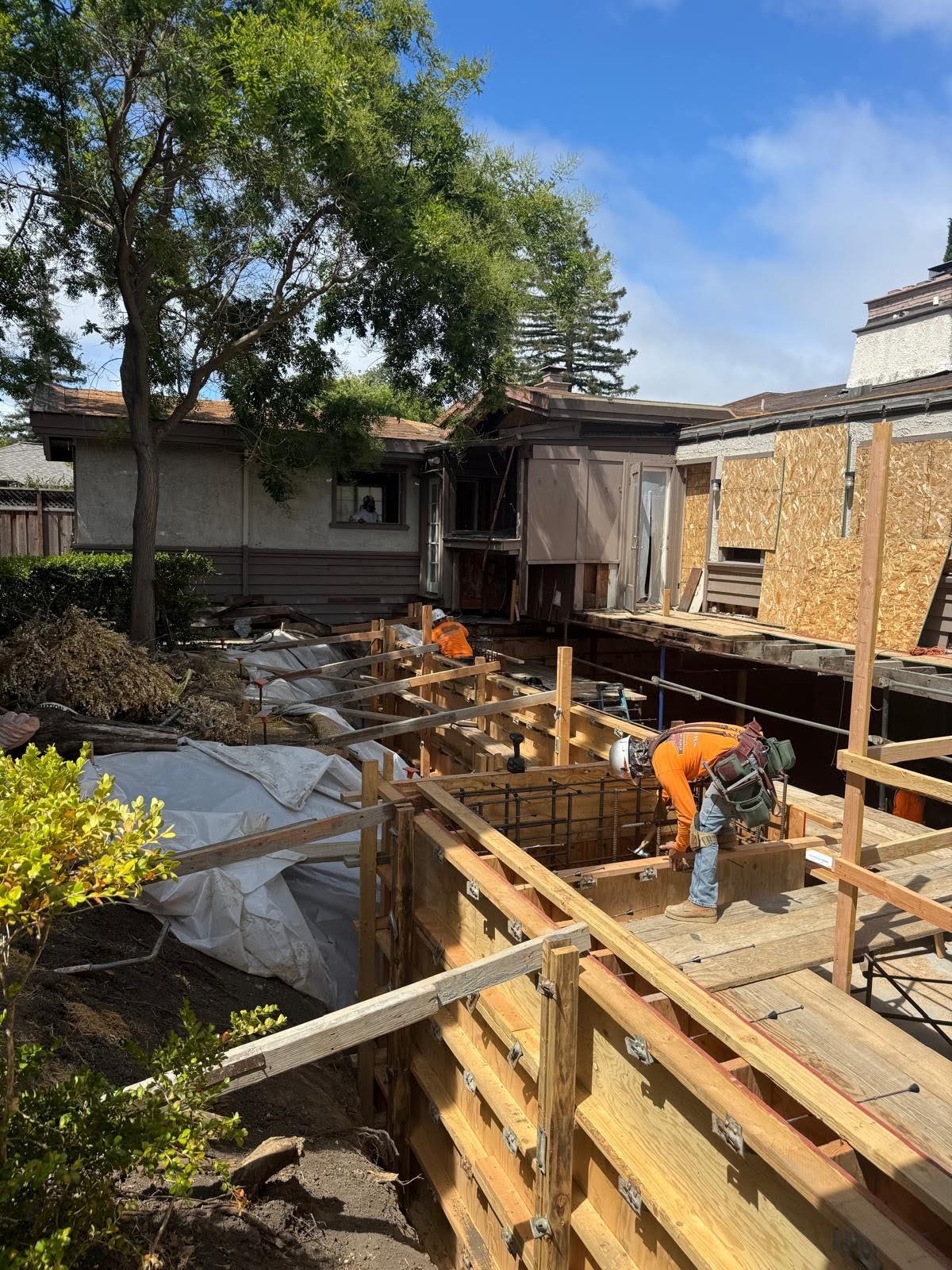 Construction crew building concrete foundation forms with rebar beside a historic Bay Area Craftsman home under renovation
