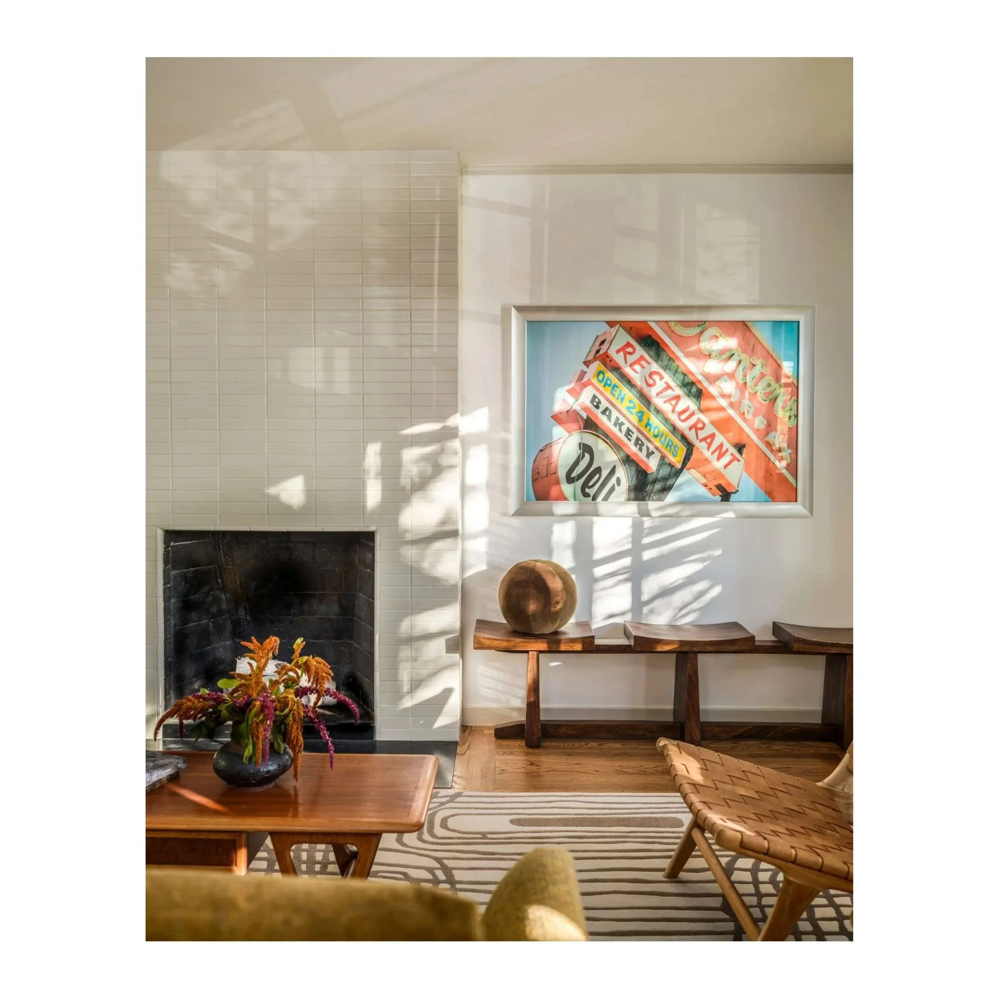 Mid-century modern living room with white tile fireplace, walnut bench, and framed vintage sign photography