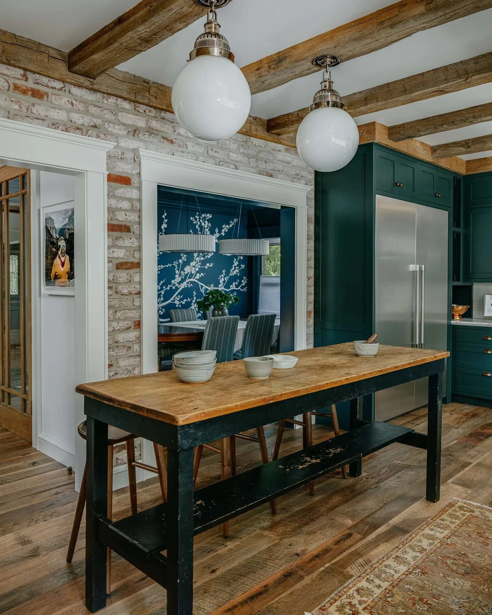 Craftsman kitchen with dark green cabinetry, exposed wood beams, and whitewashed brick archway leading to dining room