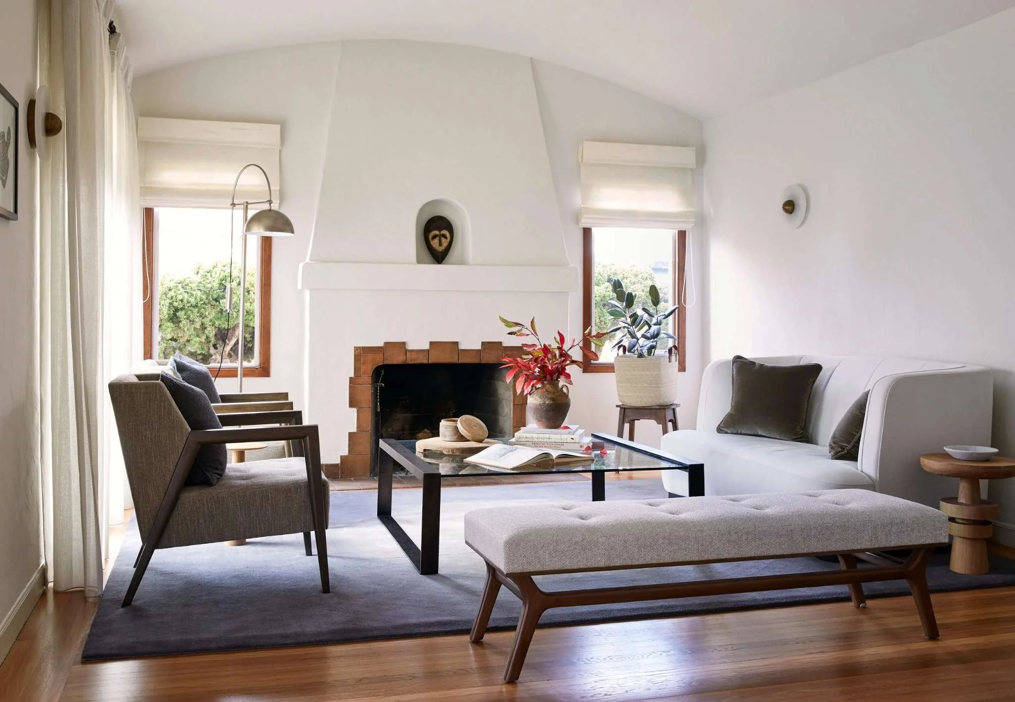 Spanish Revival living room with plaster arched fireplace, terracotta tile hearth, and African mask displayed in the niche