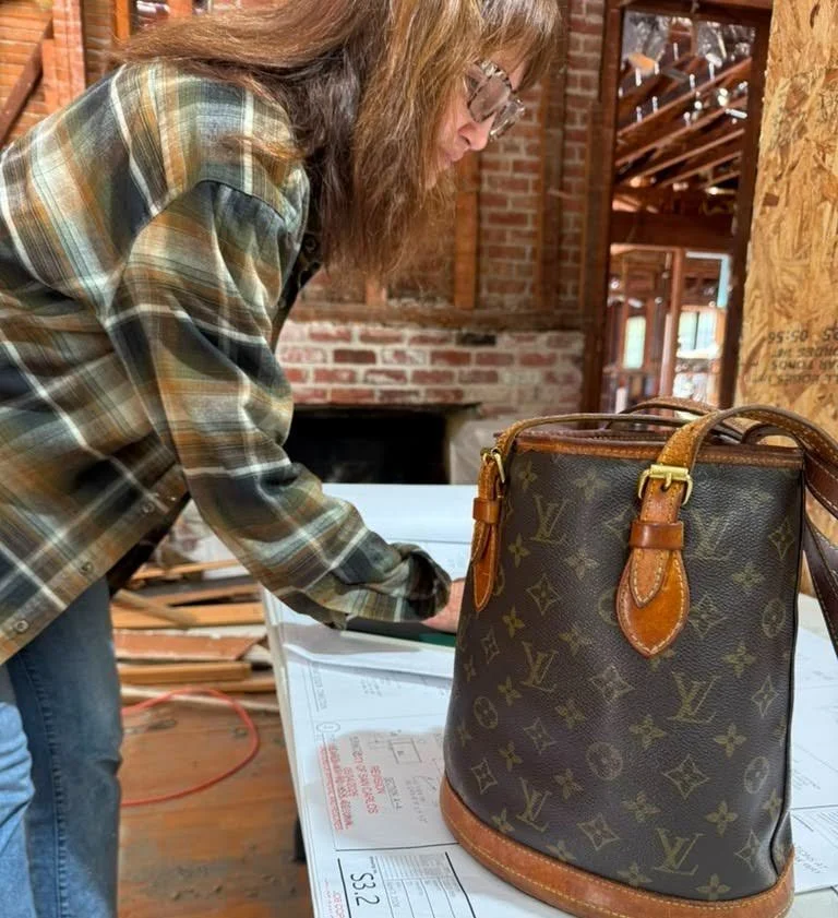 Interior designer reviewing construction plans on site in a historic home with an exposed brick fireplace and open framing