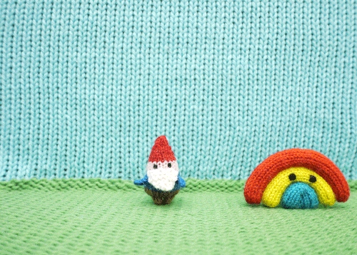 Stop motion gif of a knitted unicorn jumping over a knitted rainbow, and flying off with a knitted gnome