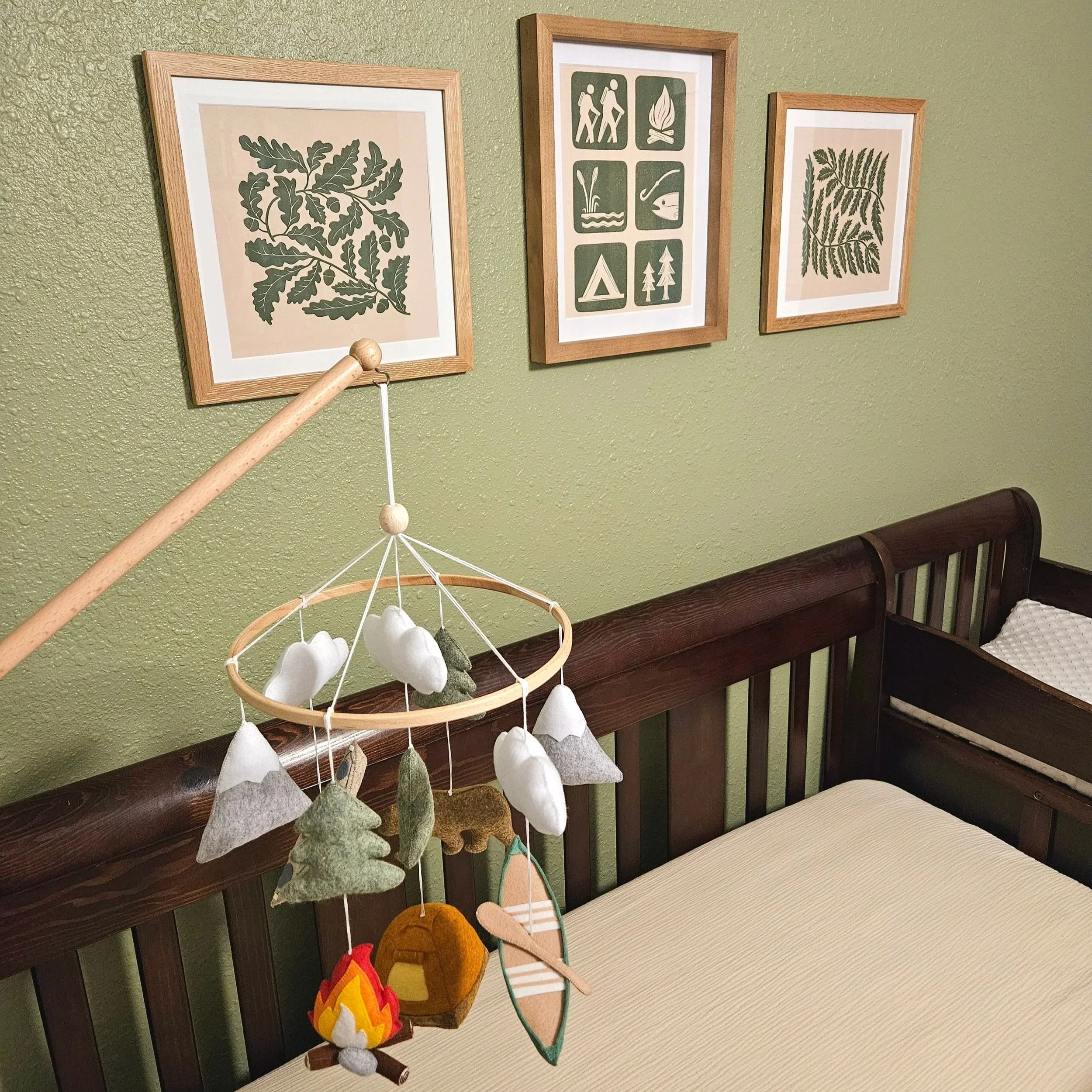 Nature inspired nursery art in olive green. Oak leaves, nature icons or national park symbols, and fern leaf art prints are displayed above a crib.