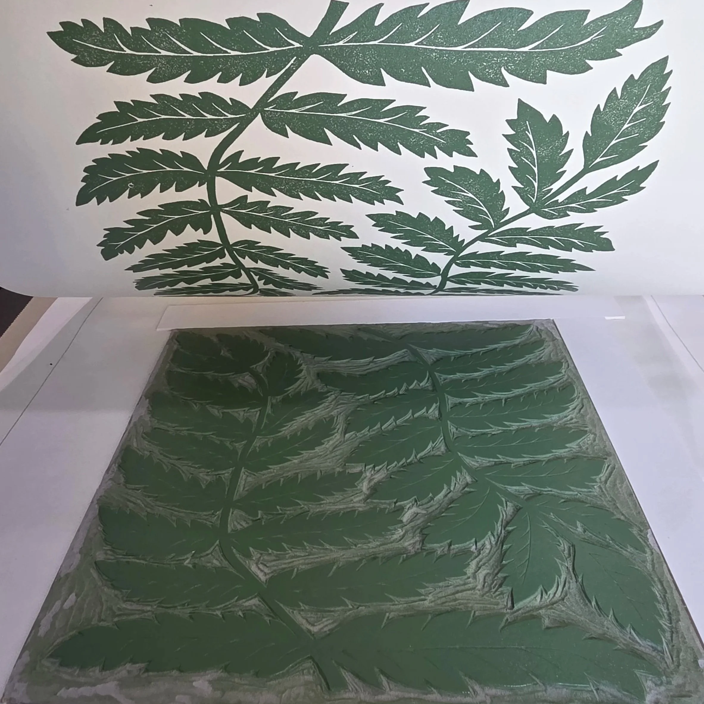Handmade block printing process showing nature-inspired fern leaves being lifted from the carved block, with olive green ink printed onto beige fine art paper.