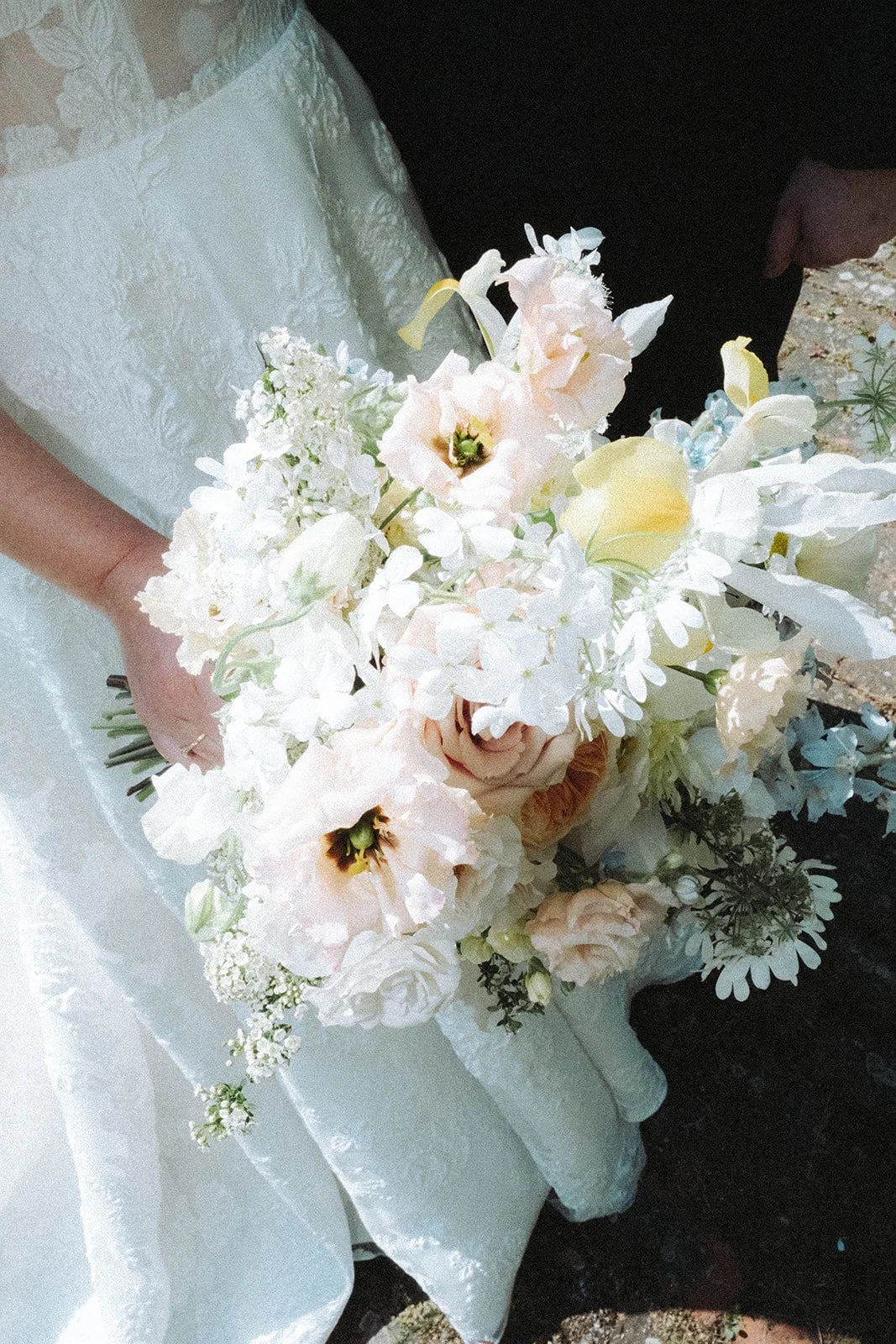 A bride holding a bouquet of white, blush, and pale pink flowers, including roses and peonies, on her wedding day. Trending floral bouquets for weddings in Norfolk and Suffolk. 