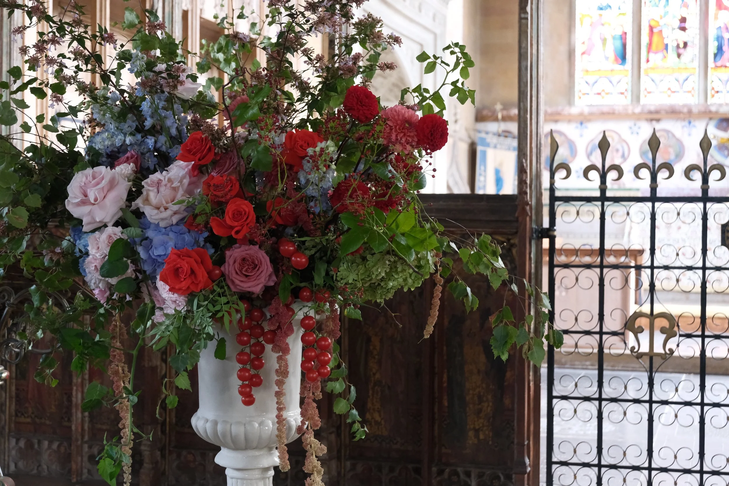 In a historic church on the North Norfolk coast. Adorned with wedding floral arrangements consisting of striking reds, blues and pinks with the fun inclusion of tomatoes.