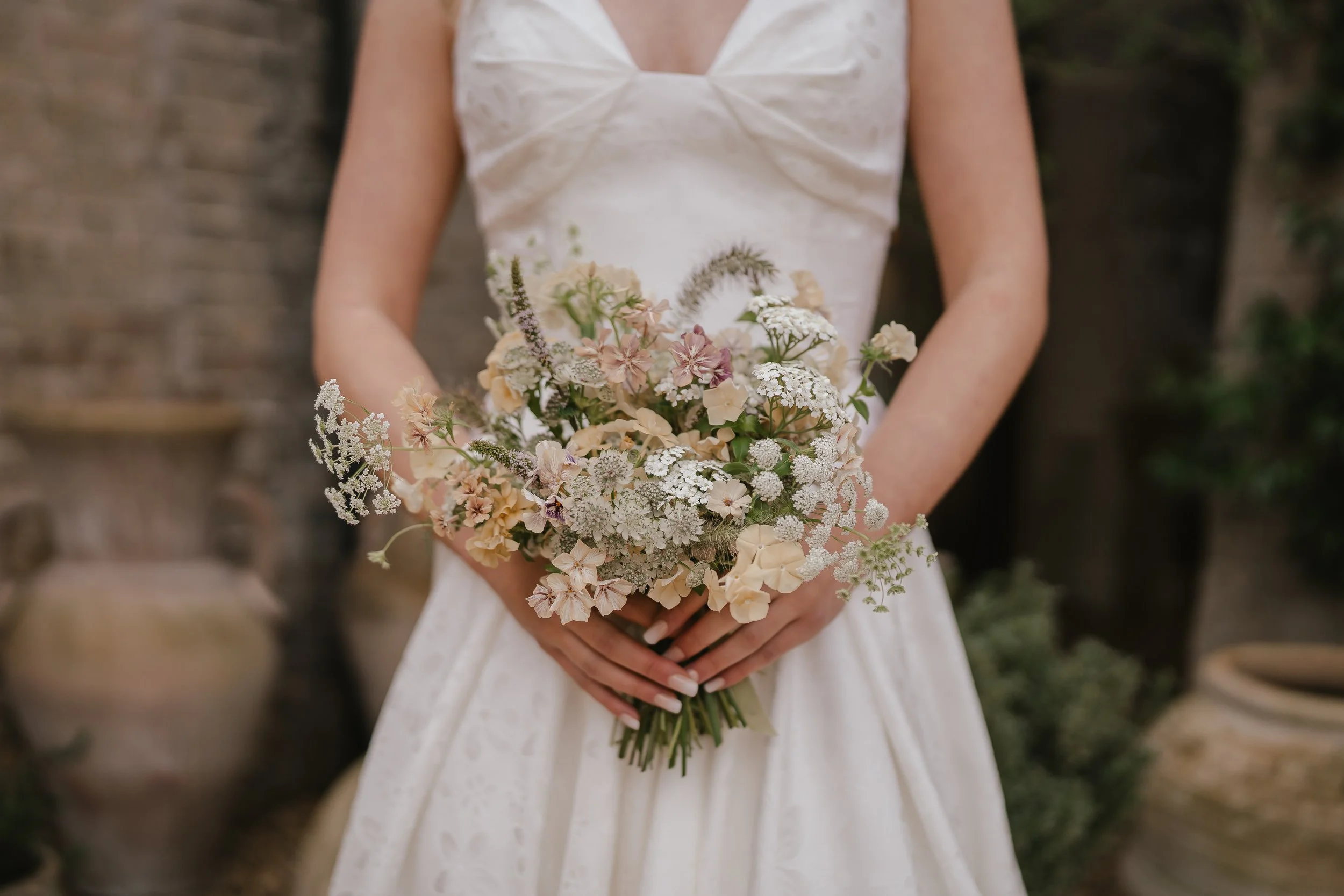 A bride holding a bouquet of pastel-colored late summer seasonal flowers, standing outdoors at Shotesham Park in Norfolk. The bouquet was curated by a Norfolk and Suffolk based wedding flower specialist. 