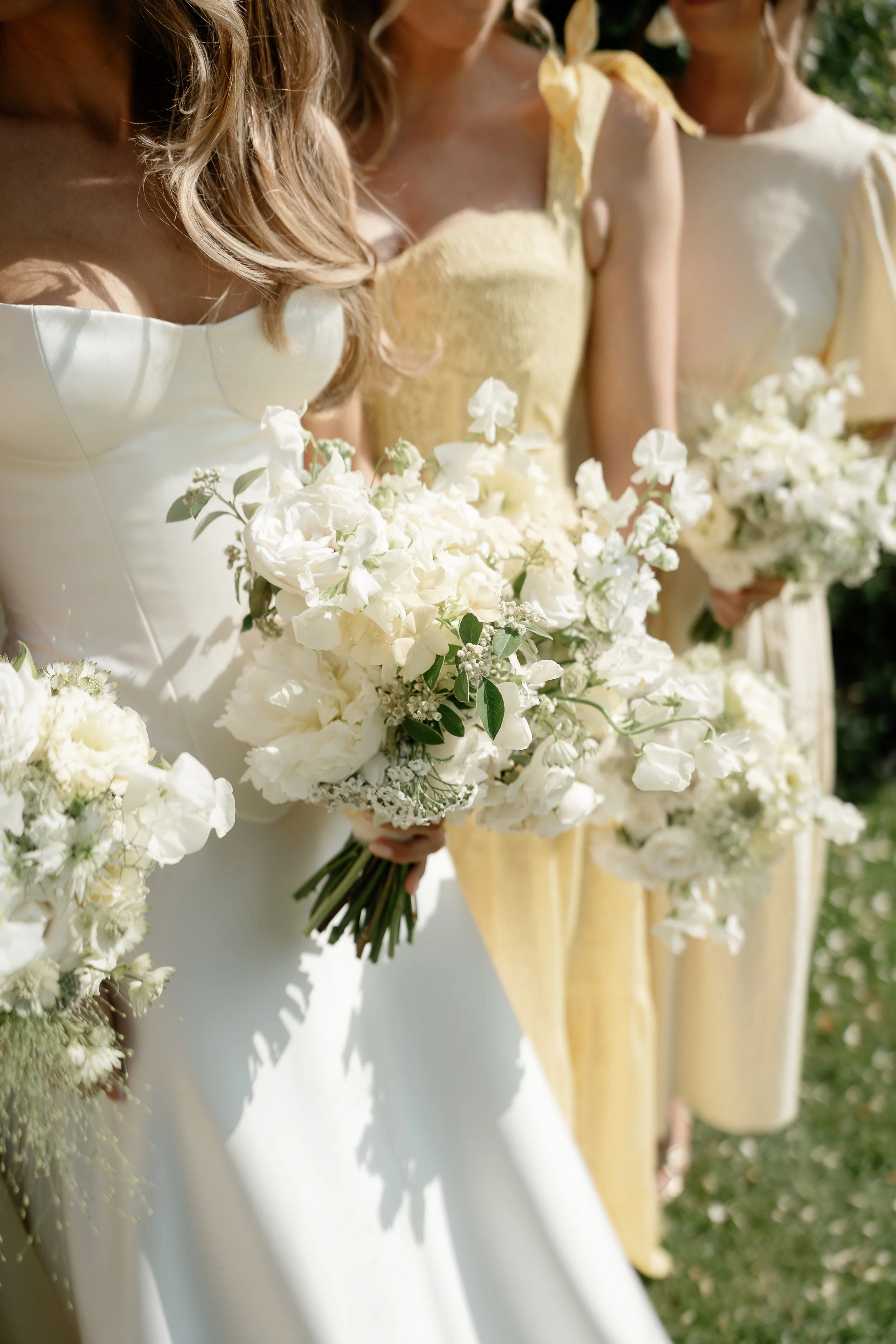 A bride and bridesmaids holding beautiful seasonal and chic white flower bouquets outdoors during a wedding ceremony in Norfolk. Photo taken by local renowned photographer Sharon Cudsworth 