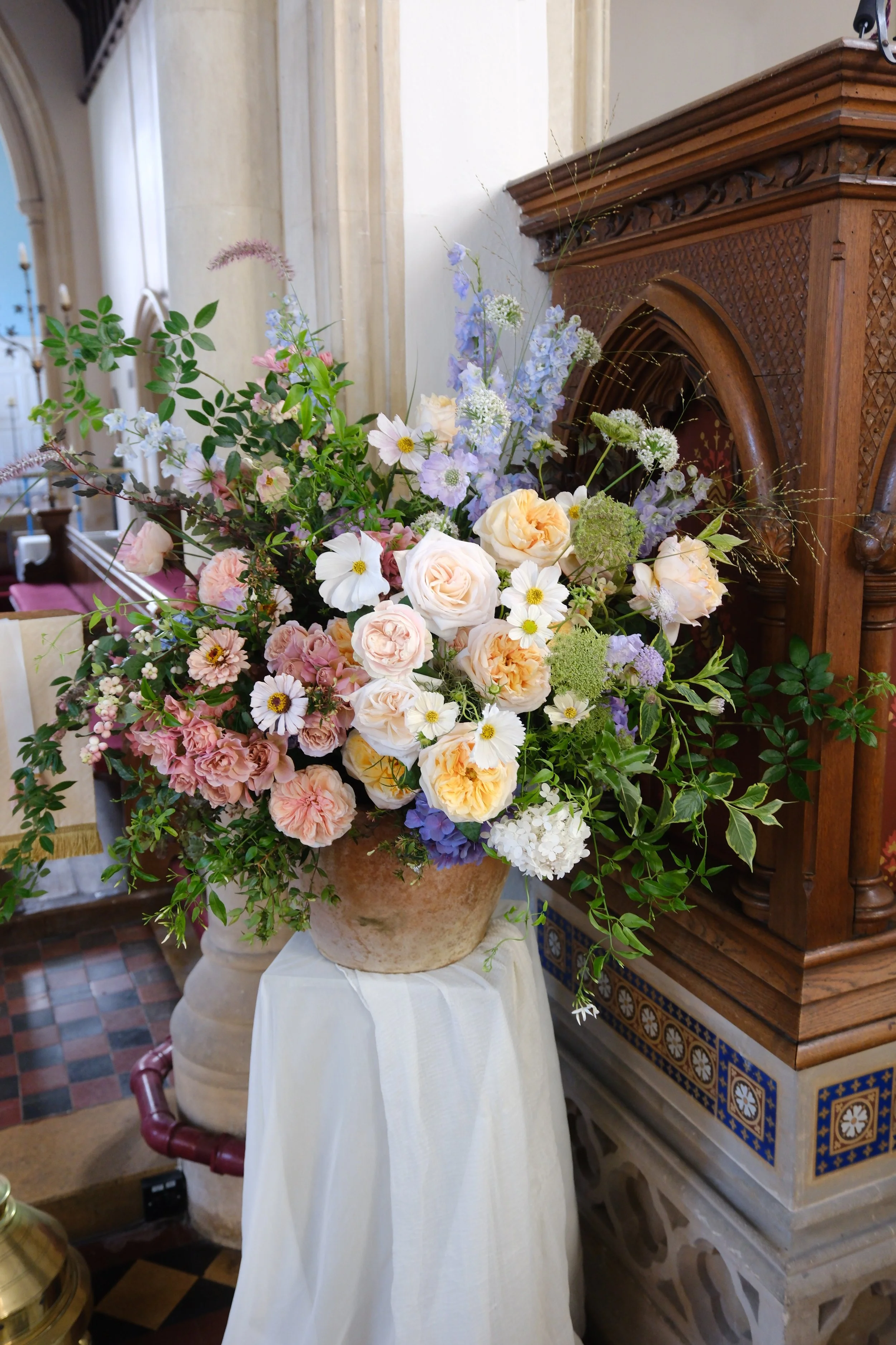 A romantic, seasonal old stone pot filled with pastel flowers for a church ceremony arrangement in Norfolk 