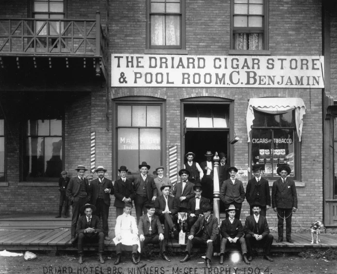 Previous to the men’s wear store Chas Benjamin owned a small cigar shop inside the Driad Hotel in Wetaskawin, Alberta. He is the well dressed fellow on the right with the dog on the leash. Not only could he sport a cowboy hat, but he was pretty dapper as well.