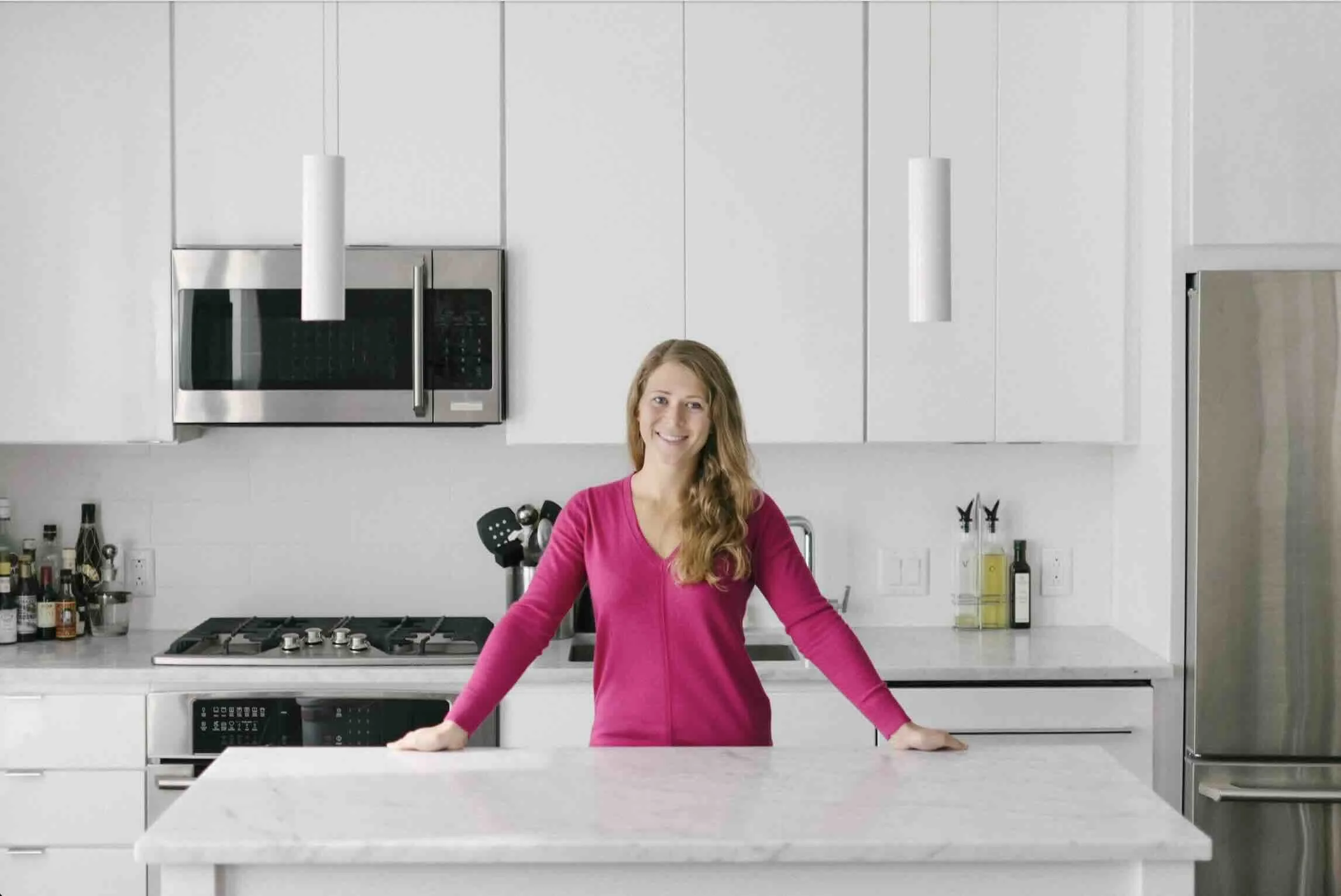 Emily Arkin, MS, RD, LD, CSDH smiling in front of a glossy white kitchen with stainless steel appliances