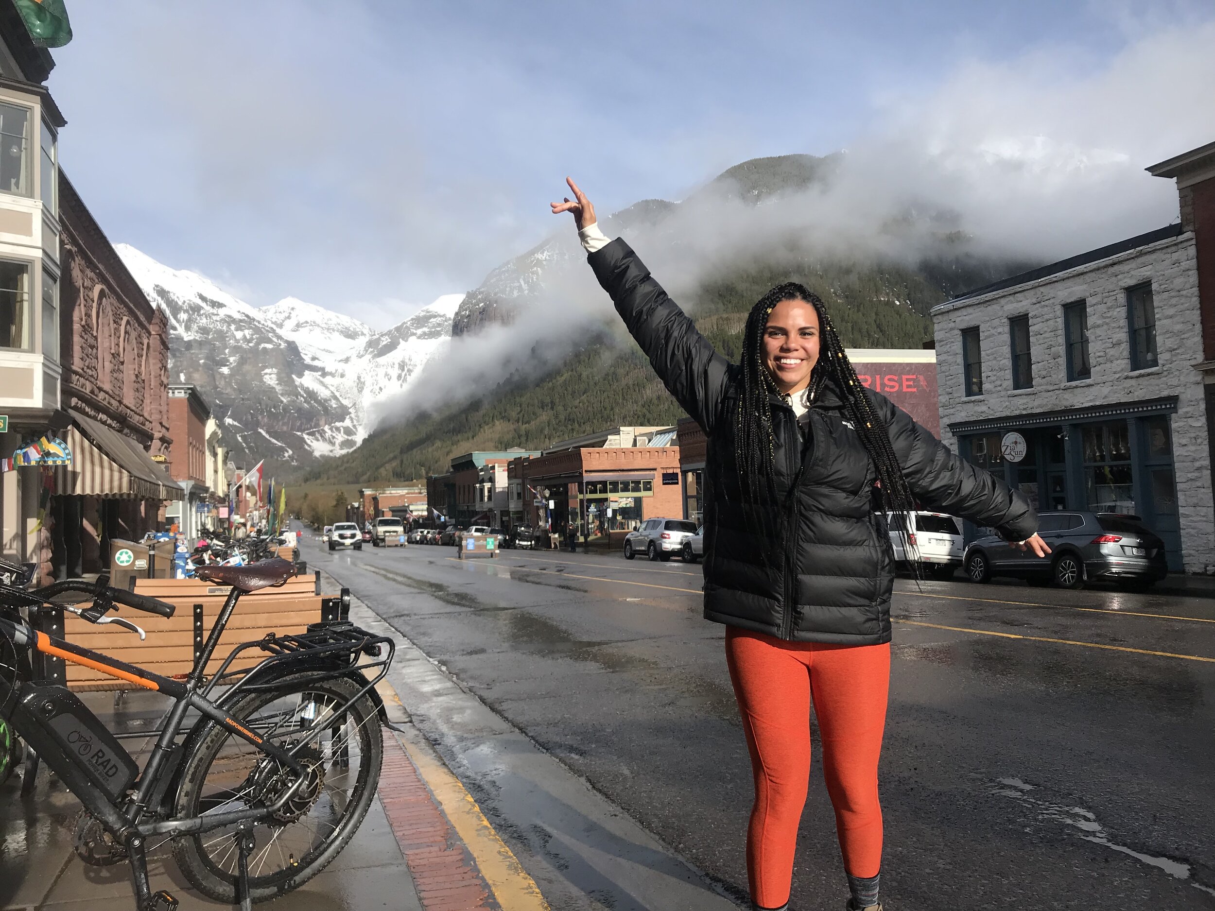 The author, seen in a black puffy jacket and brightly colored tights in downtown Telluride, CO on occupied Ute land. (Photo credit: Jenny Bruso)