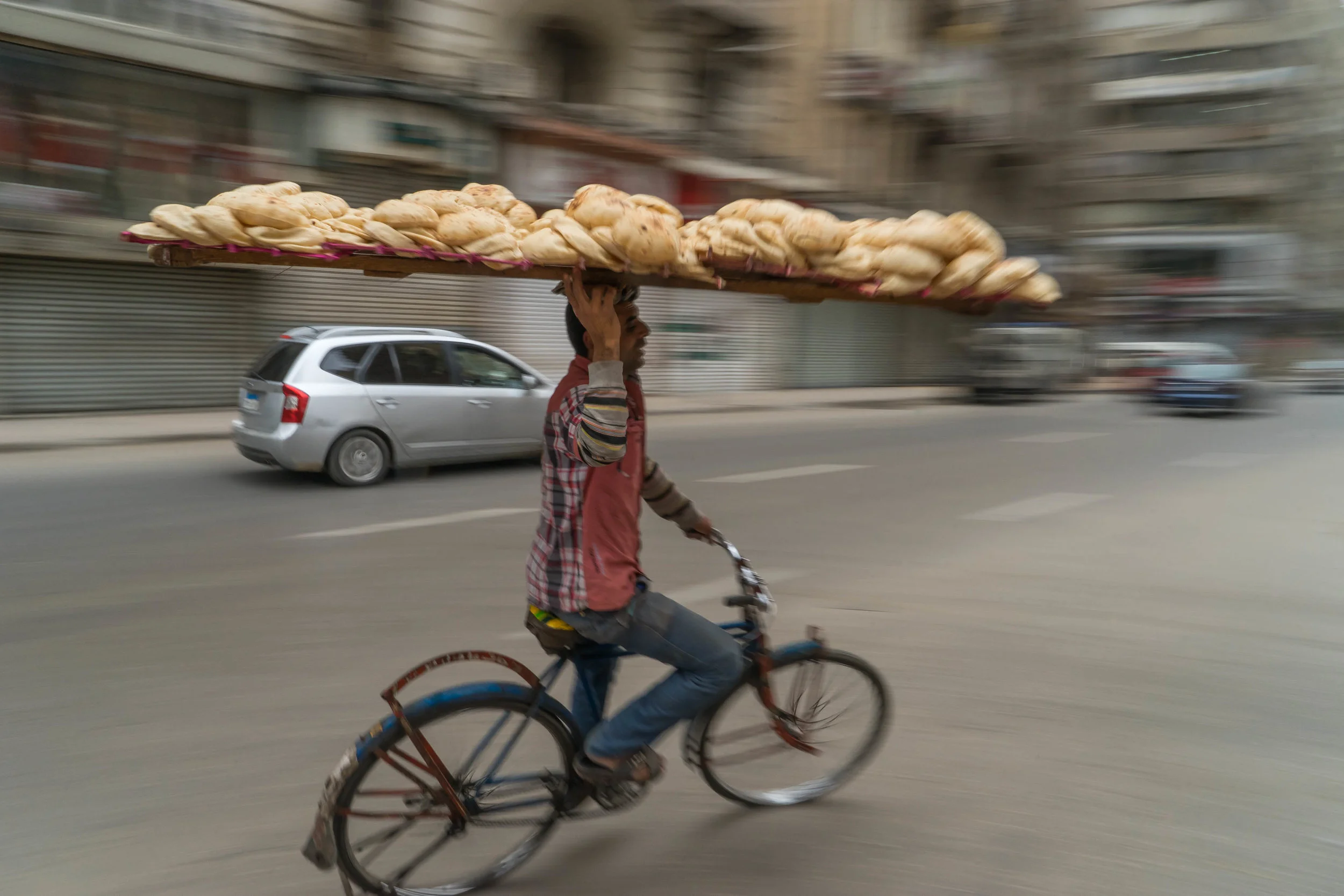 A man delivers bread on his head through the traffic of Cairo, Egypt. 2017.