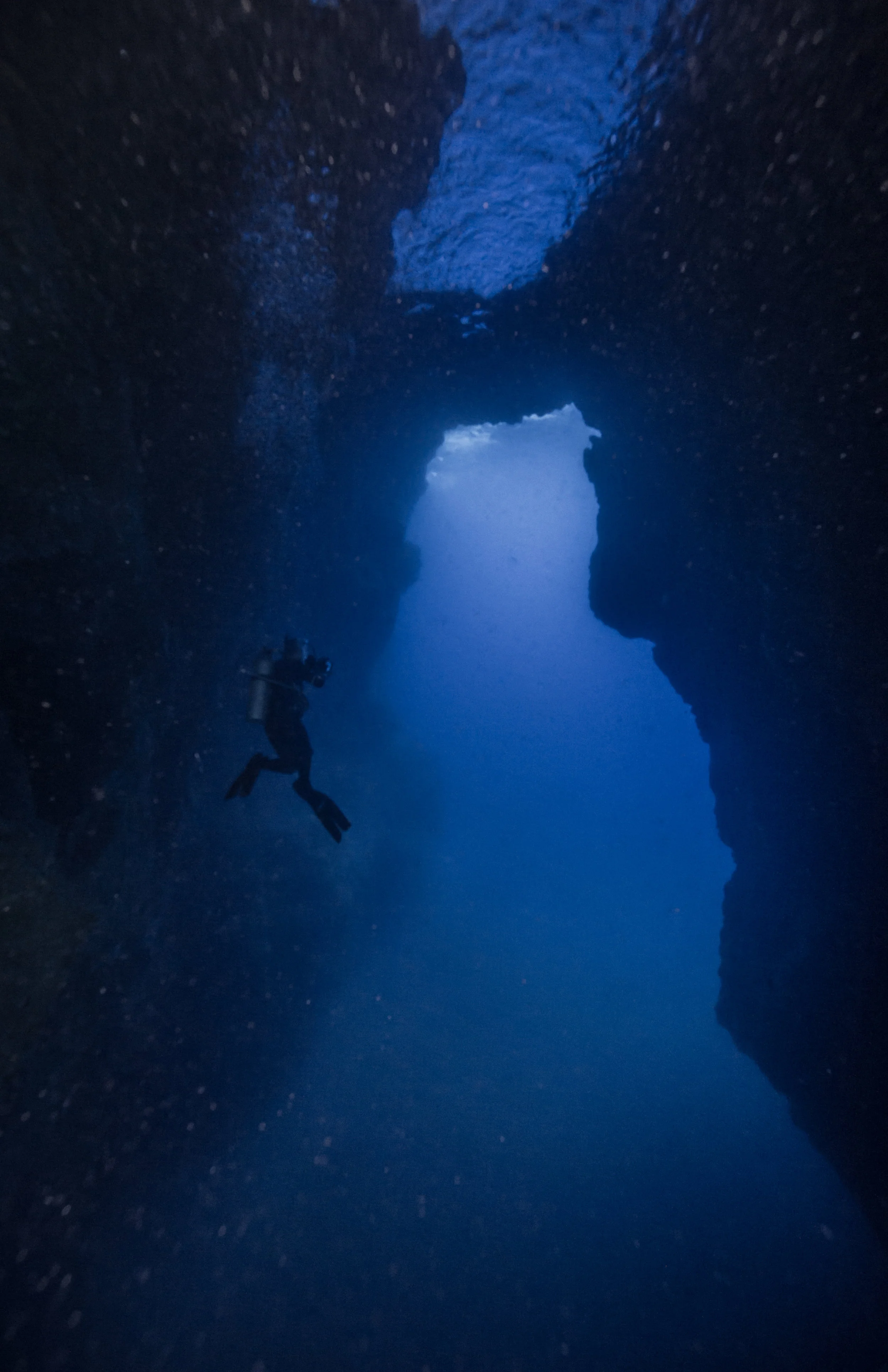 A diver, towered by an air pocket, stops to take a picture of a swim-through arch underneath an offshore island in Molokai, Hawai'i. 2017.
