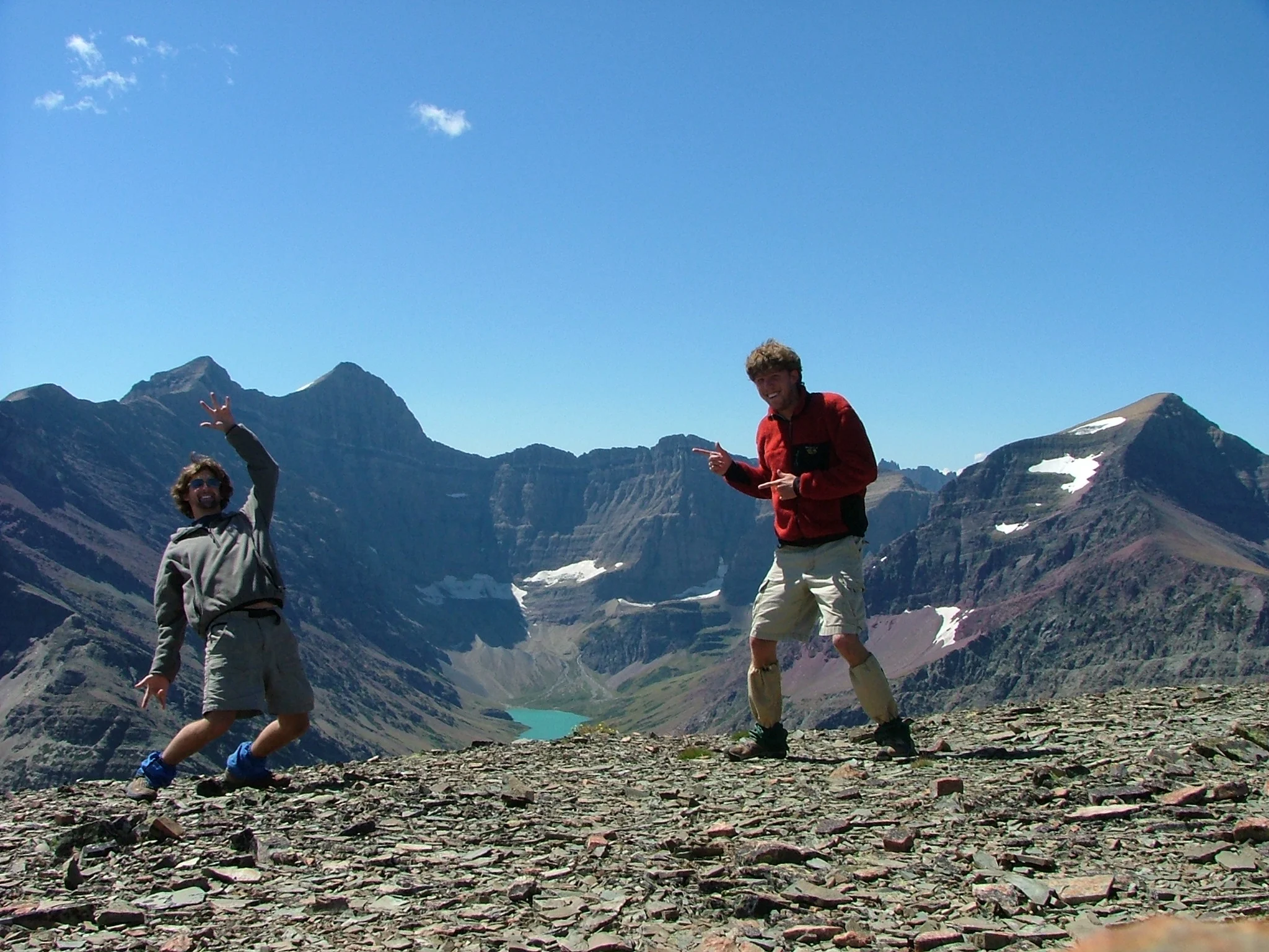 A pair of callow young mountaineers encourage you to “Rock On” while following the long, long ridge from Mt. Wynn to Mt. Siyeh in the distance. Cracker Lake peaks up at the base of Siyeh in the middle of the photo.