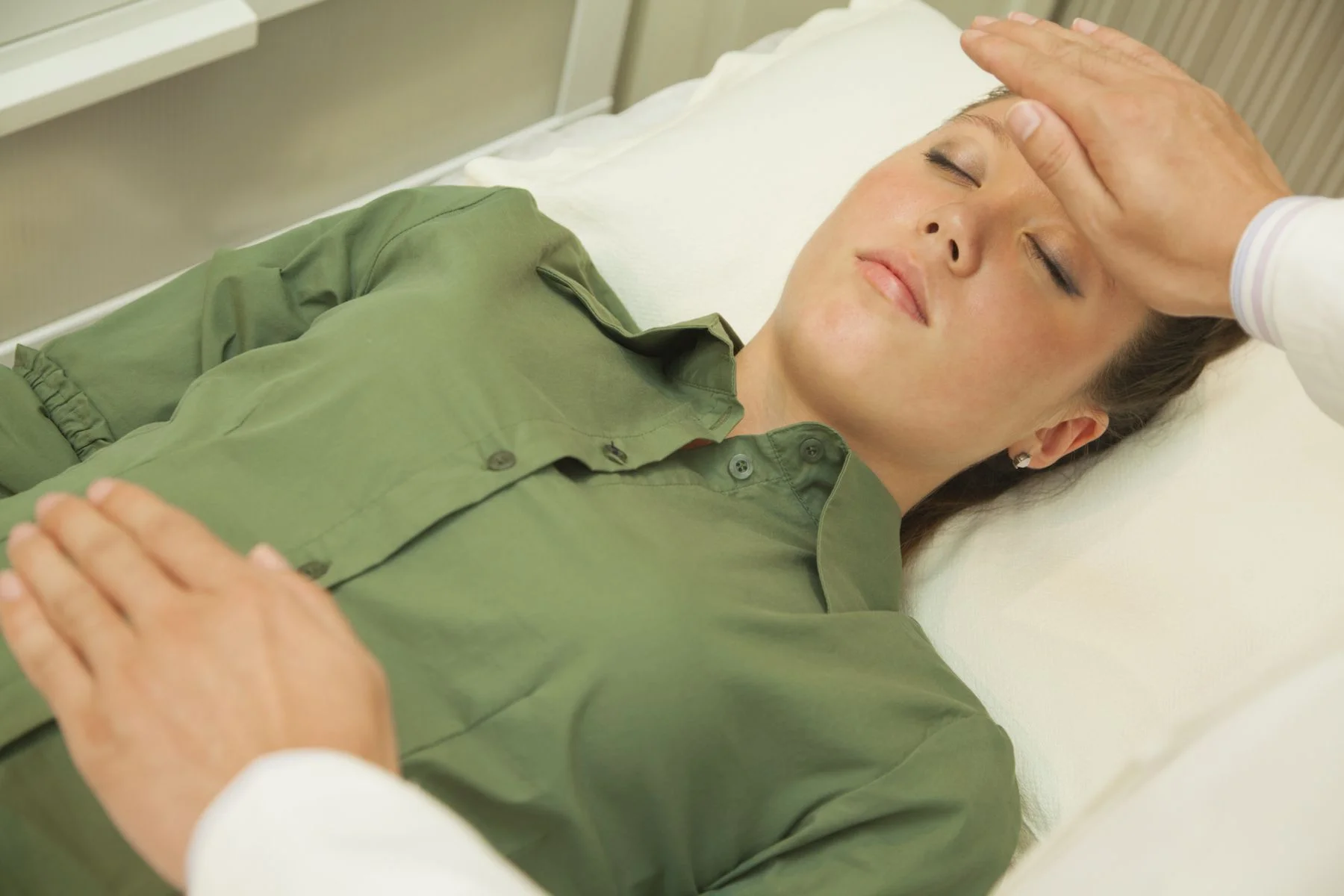 Reiki practitioner placing hands gently on a client's forehead during a treatment