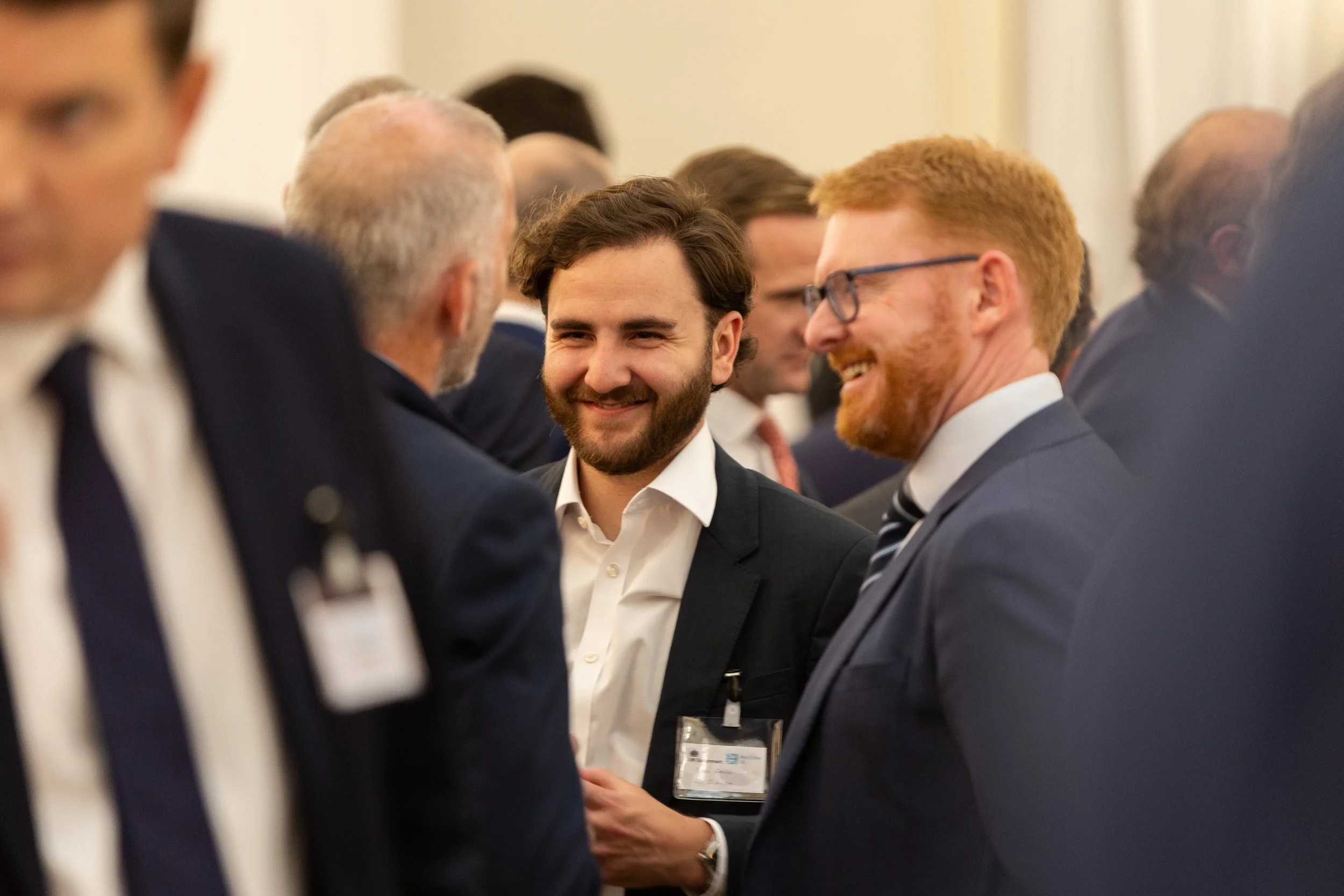 Group of men in suits talking and smiling at a professional event or conference.