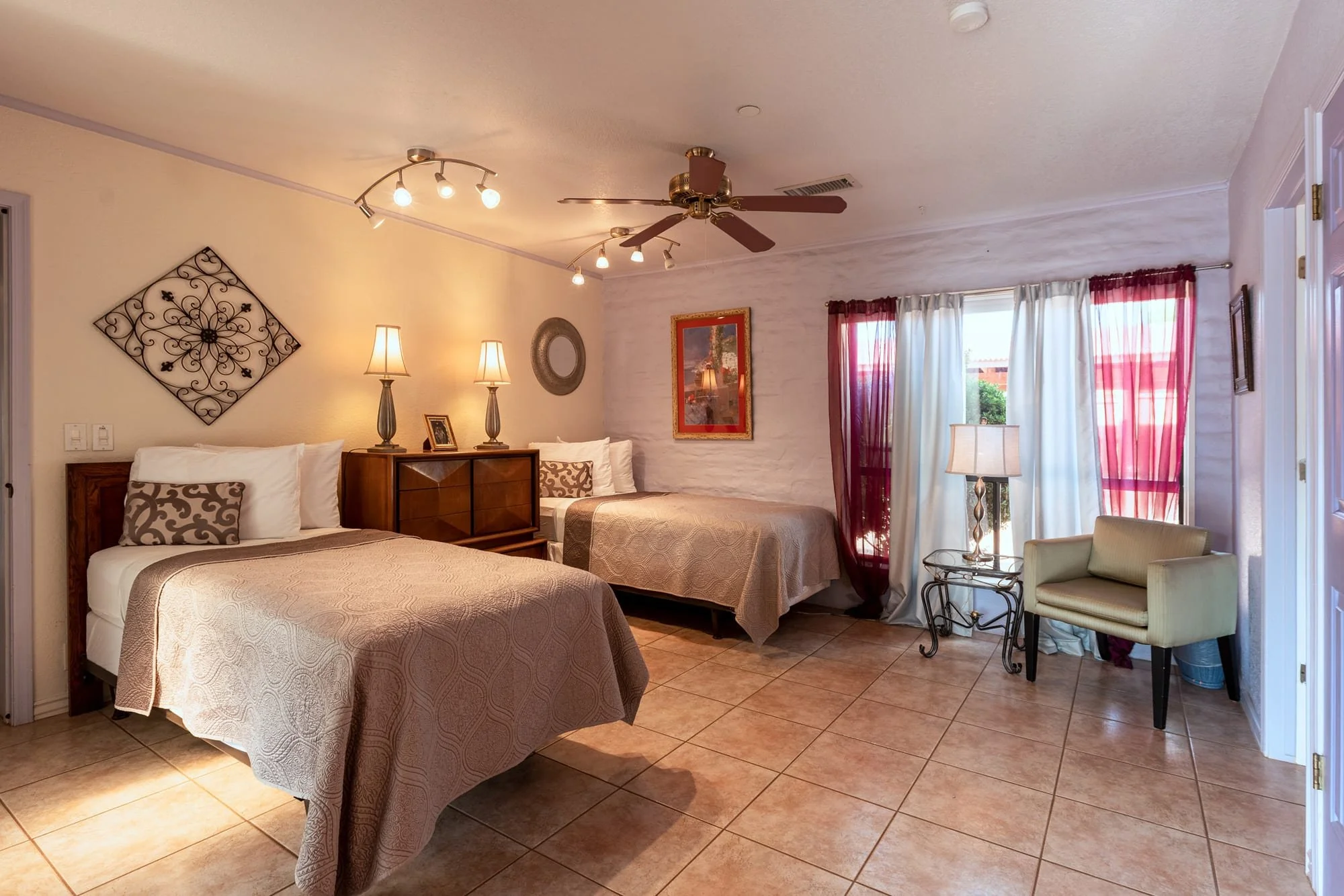 A bedroom with two beds, a window with curtains, lamps, and decorative wall art.