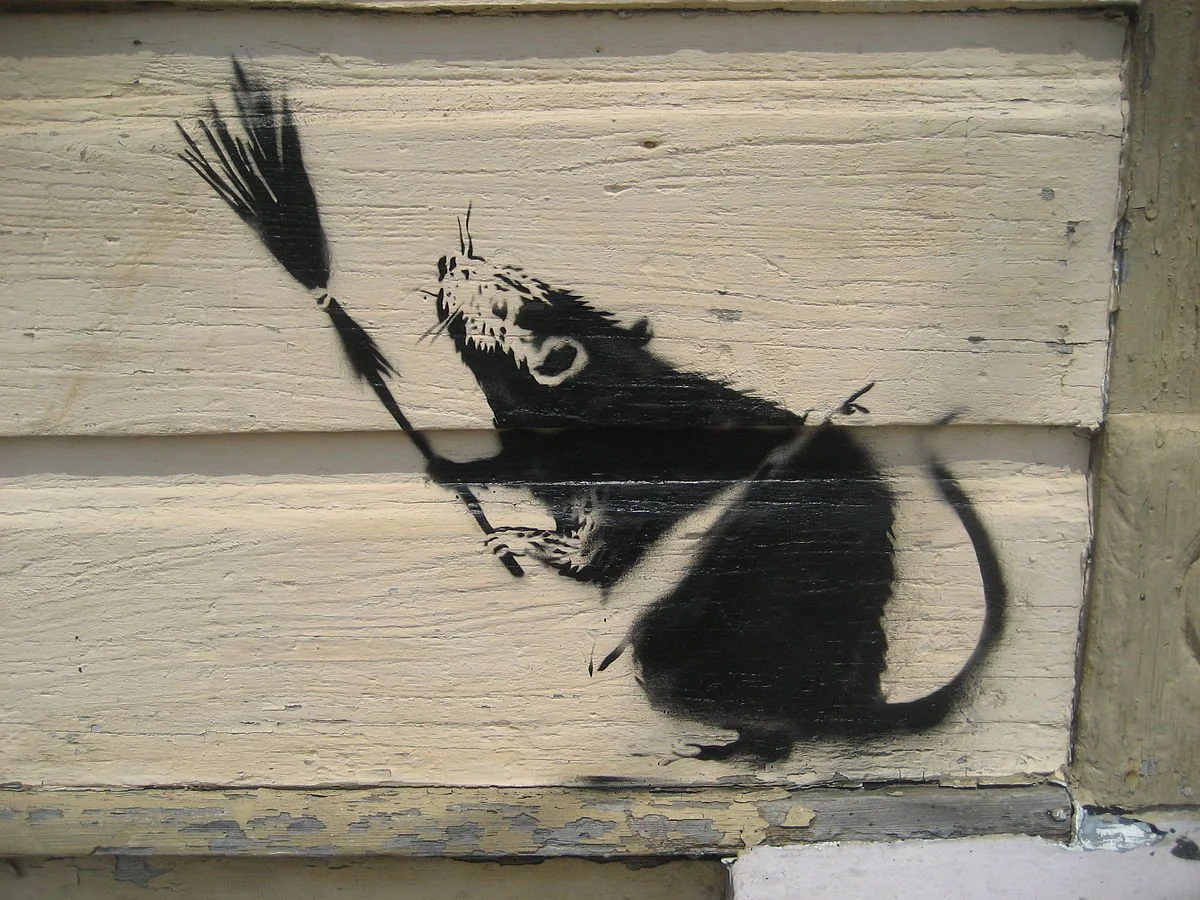 An image of a spray painted, black rat holding a broom and looking up.