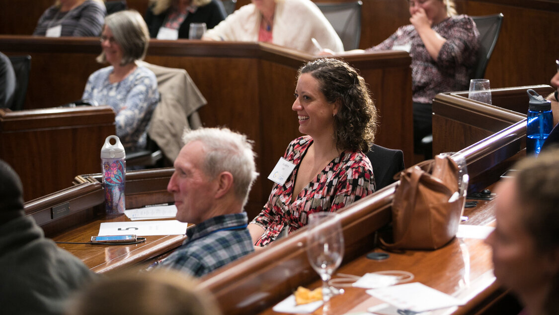 People sitting and smiling in legislative chambers