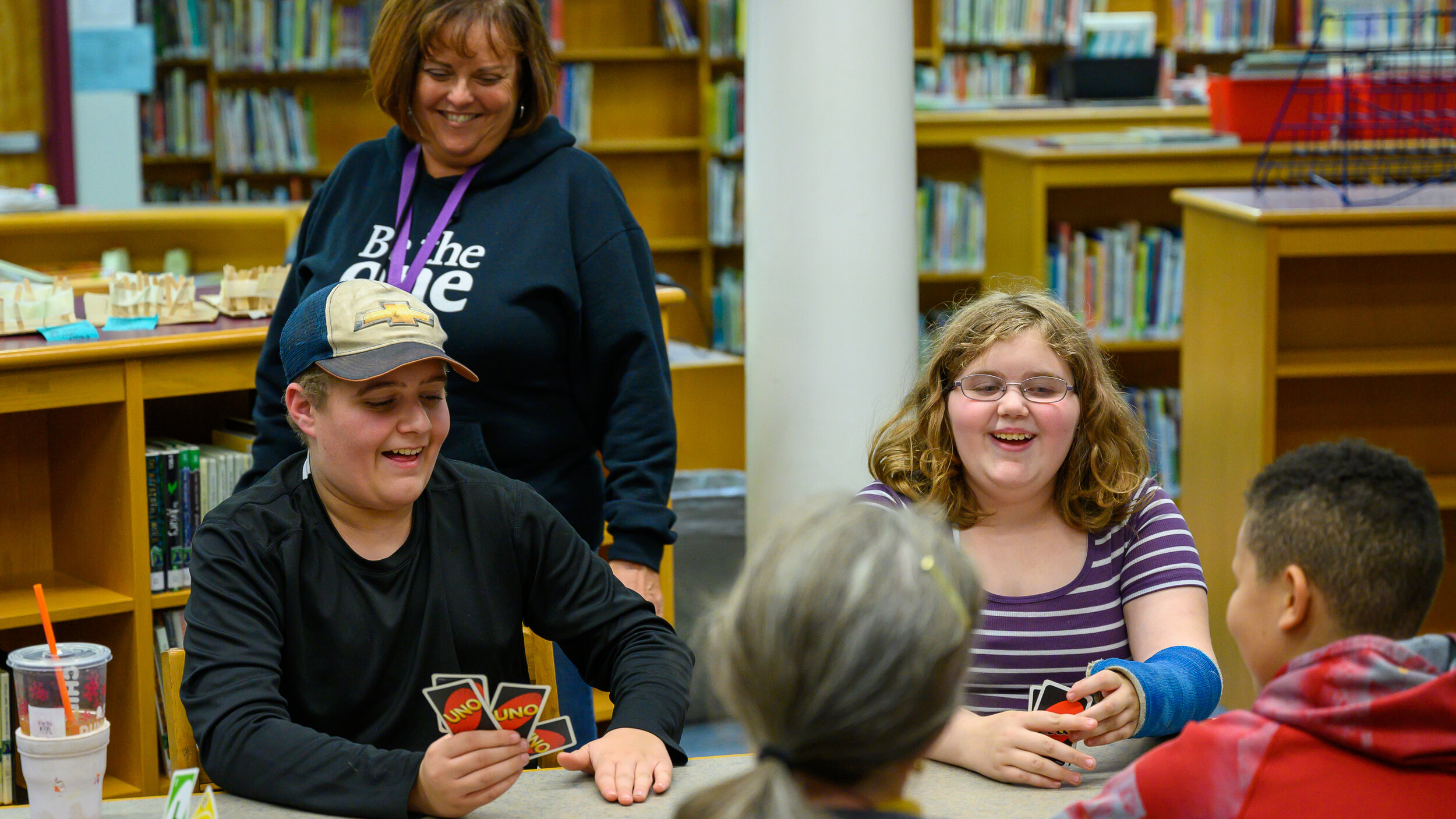 Children play a card game in a library supervised by adults