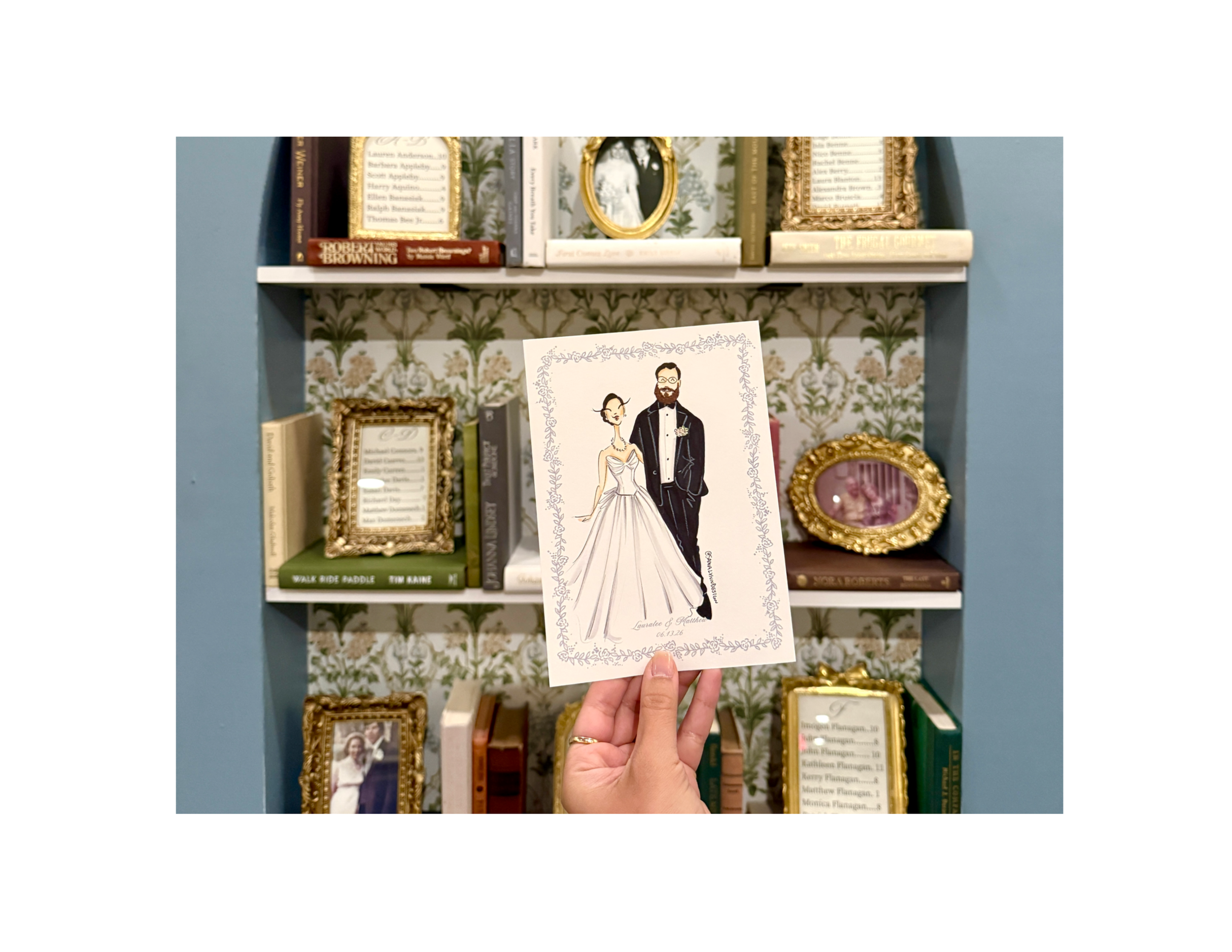 A woman holds a custom sketch of a bride and groom in front of a bookcase with gold frames