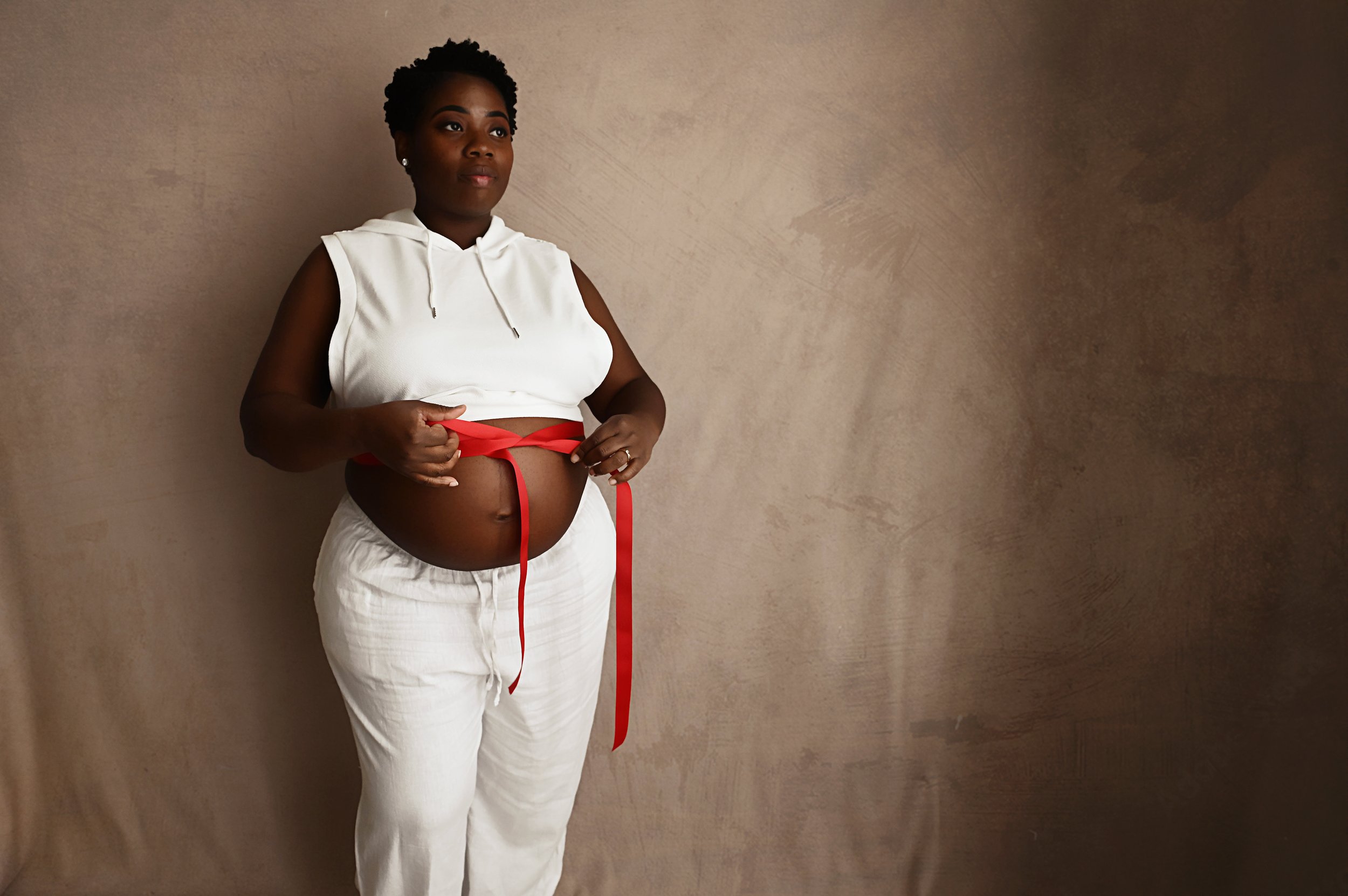 pregnant mother tying red ribbon around baby bump during maternity photography session
