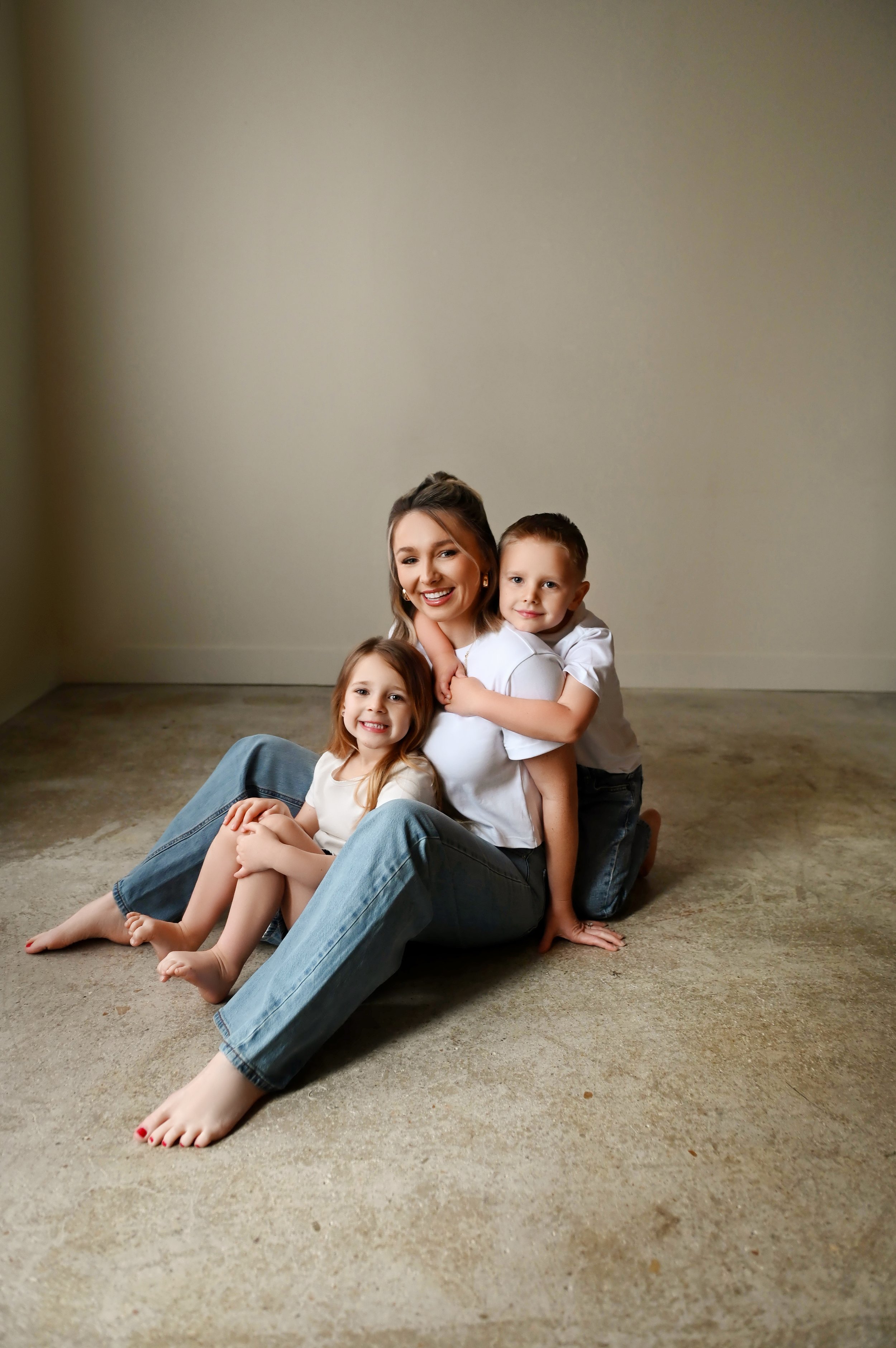 mom sitting on floor hugging young son and daughter during motherhood photography session