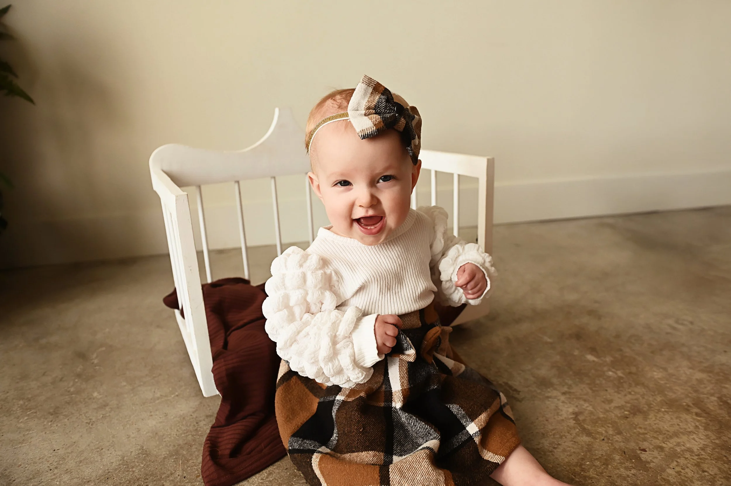 baby girl milestone photography sitting beside white crib prop in studio