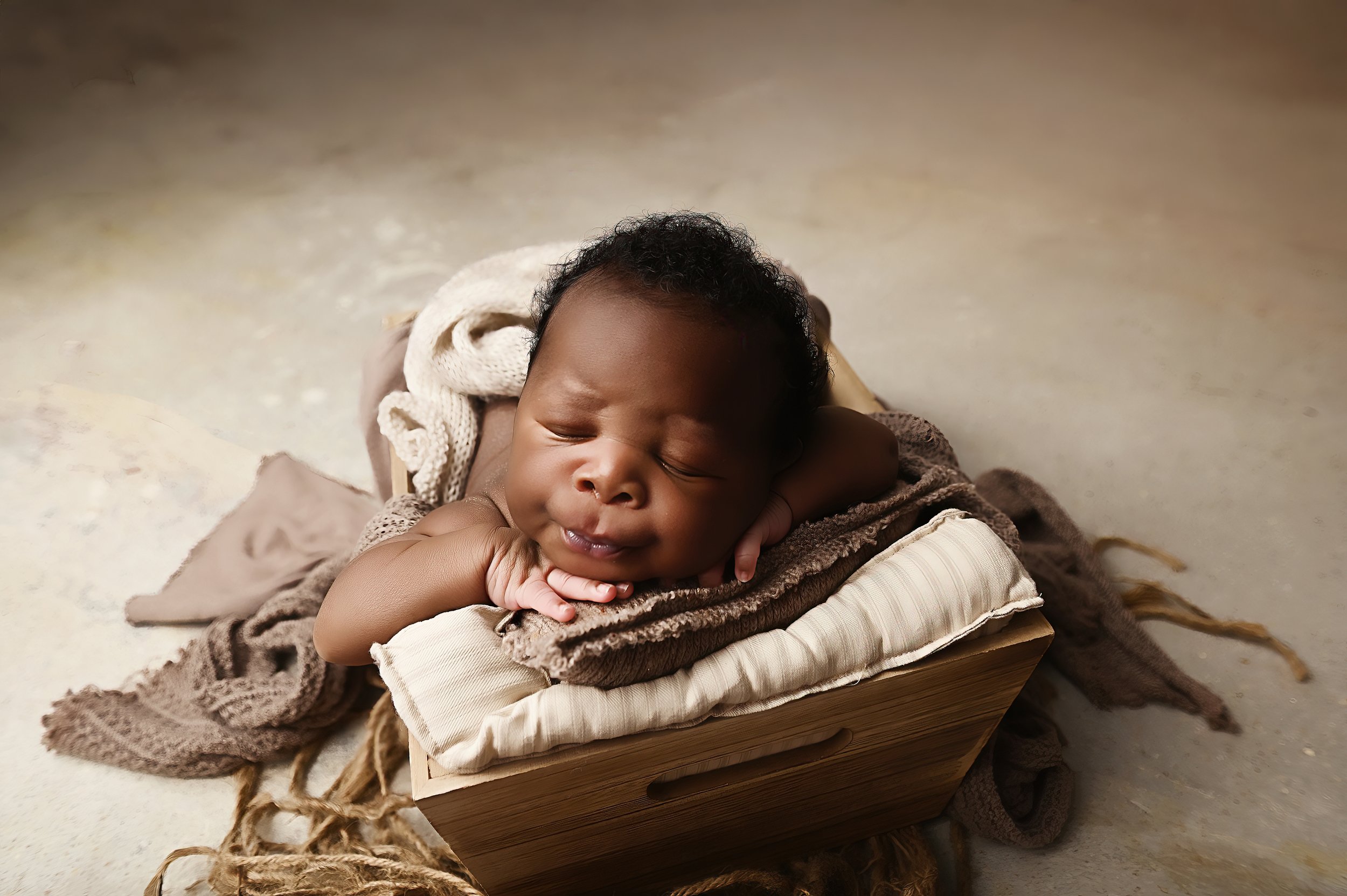 Newborn baby sleeping on folded neutral fabrics inside a wooden box during a Shreveport studio newborn session.