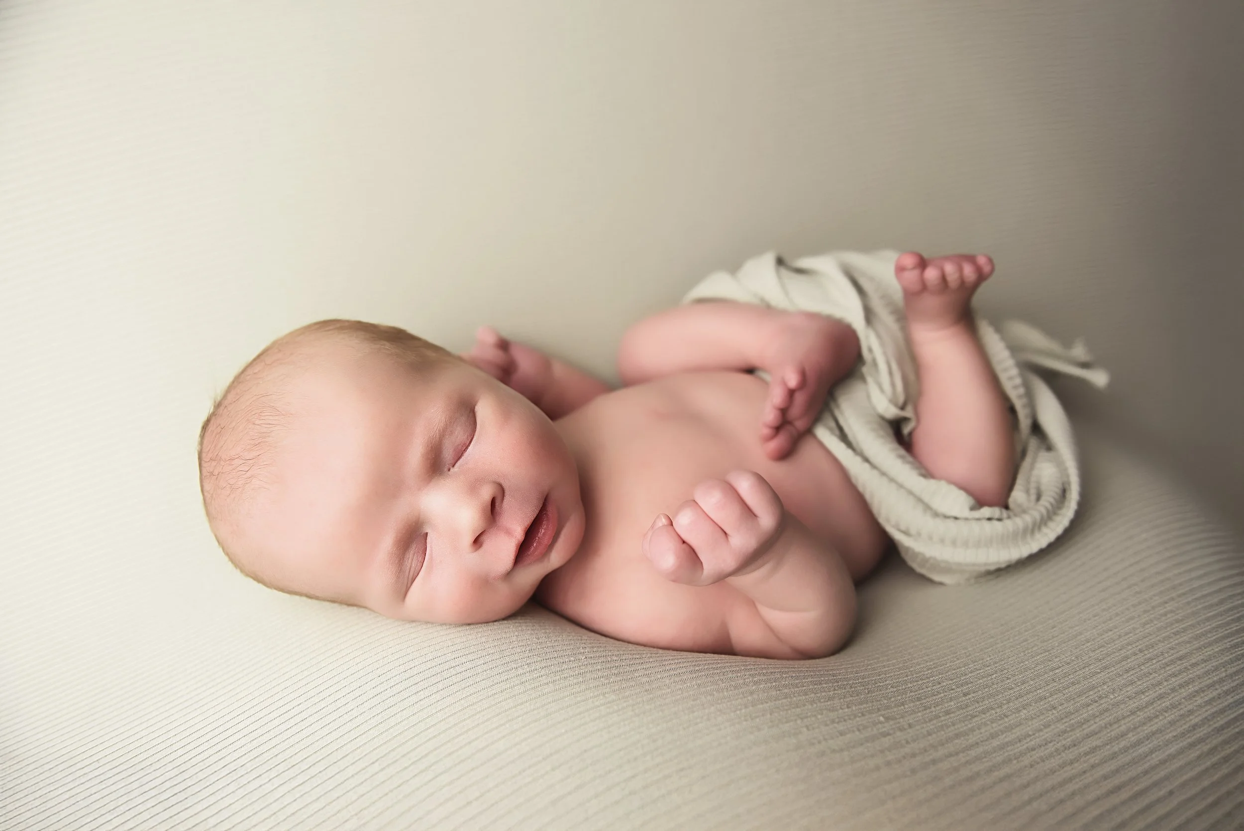 Newborn smiling and stretching on cream backdrop