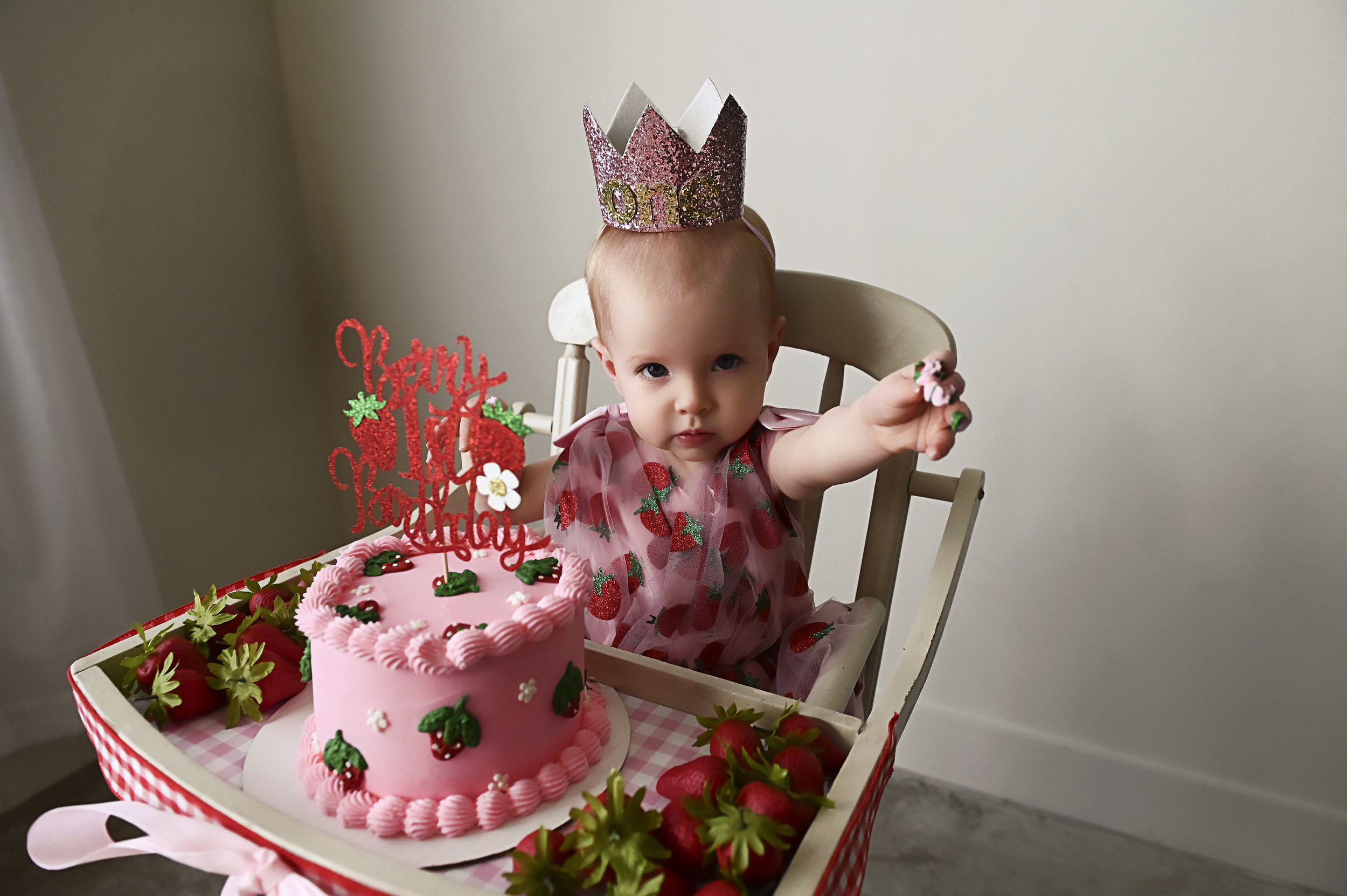 baby girl in high chair with strawberry cake and one birthday crown