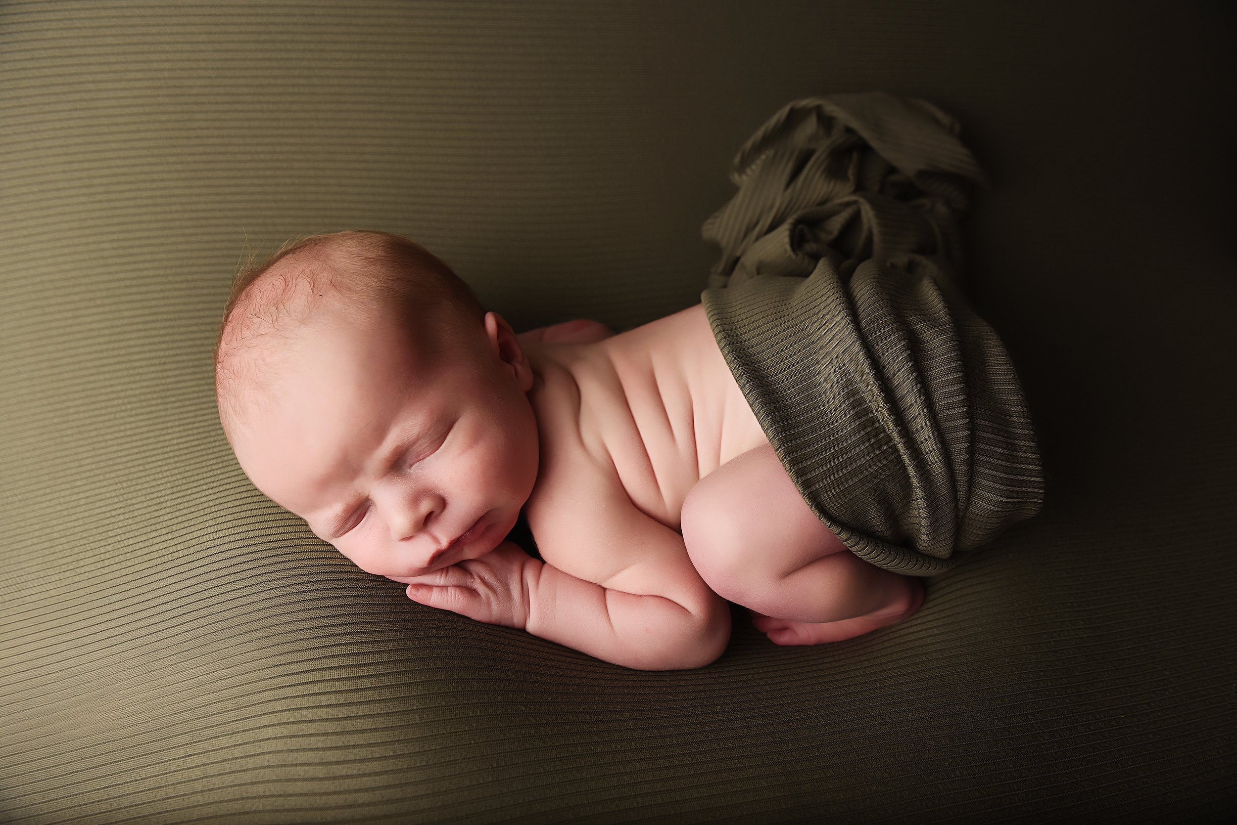Studio newborn curled pose with green ribbed wrap