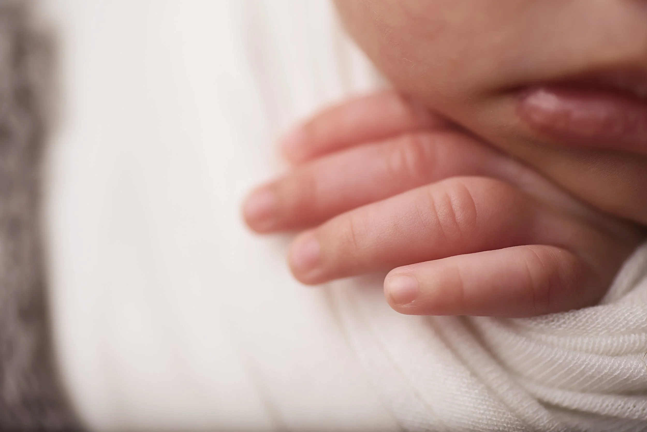 Close-up of a newborn baby’s fingers resting on her swaddle
