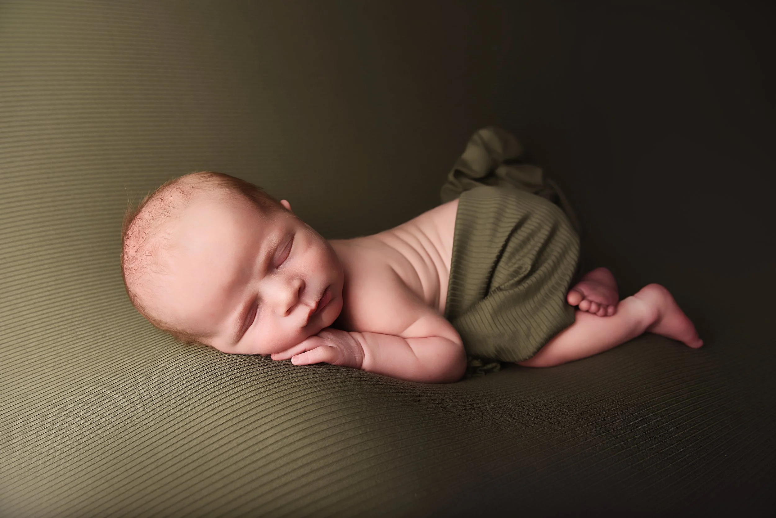 Newborn baby boy sleeping on moss green backdrop in studio