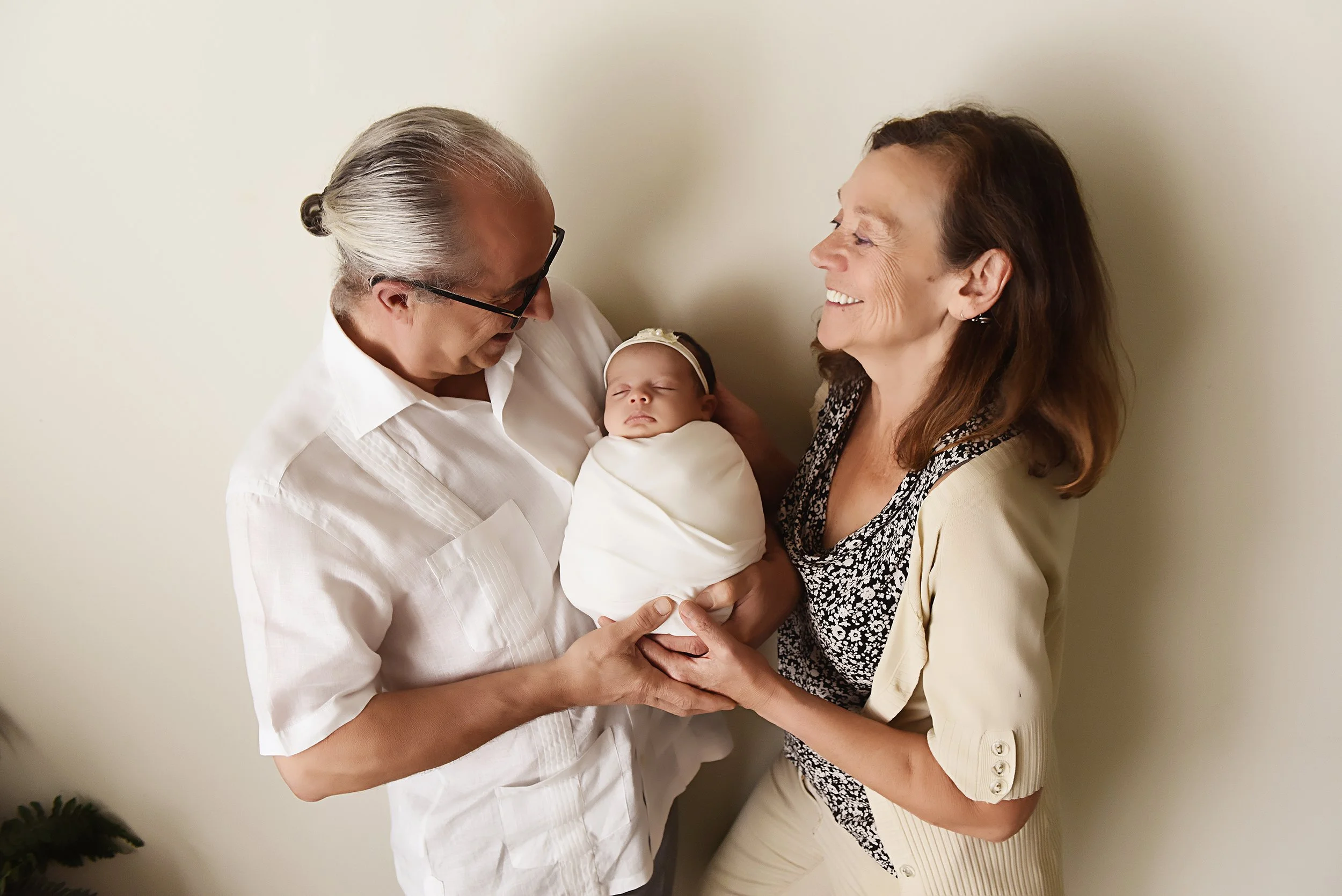 Newborn baby girl swaddled in white, lovingly held by her Italian grandparents