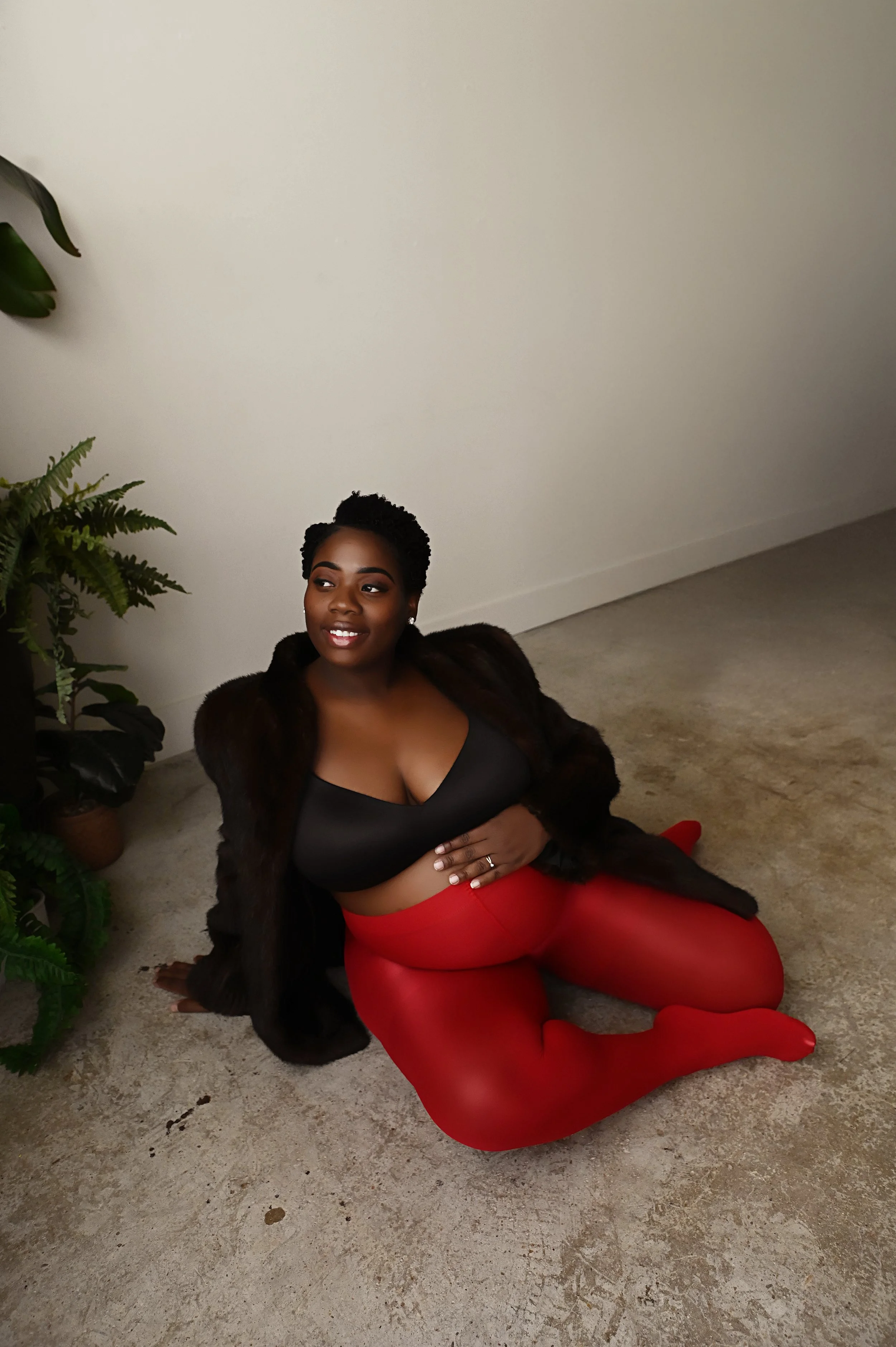 pregnant woman sitting on studio floor wearing red tights and black wrap during editorial maternity portrait