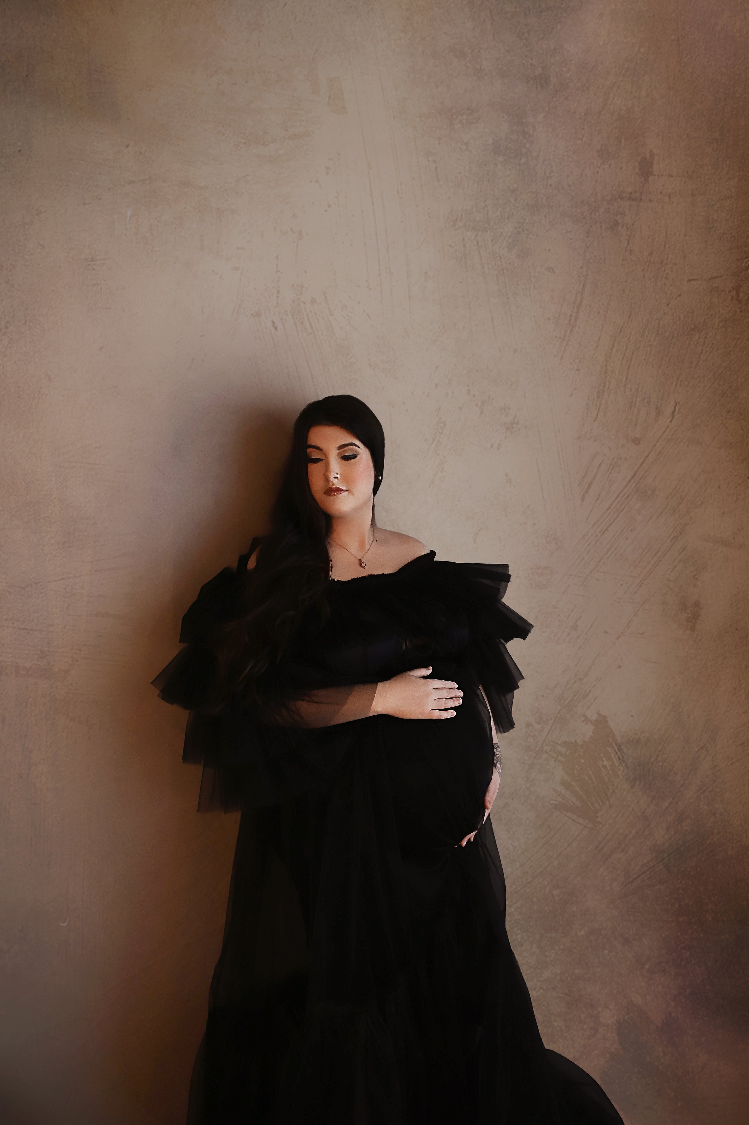 Studio maternity session in Shreveport featuring a pregnant woman in a black gown near window light
