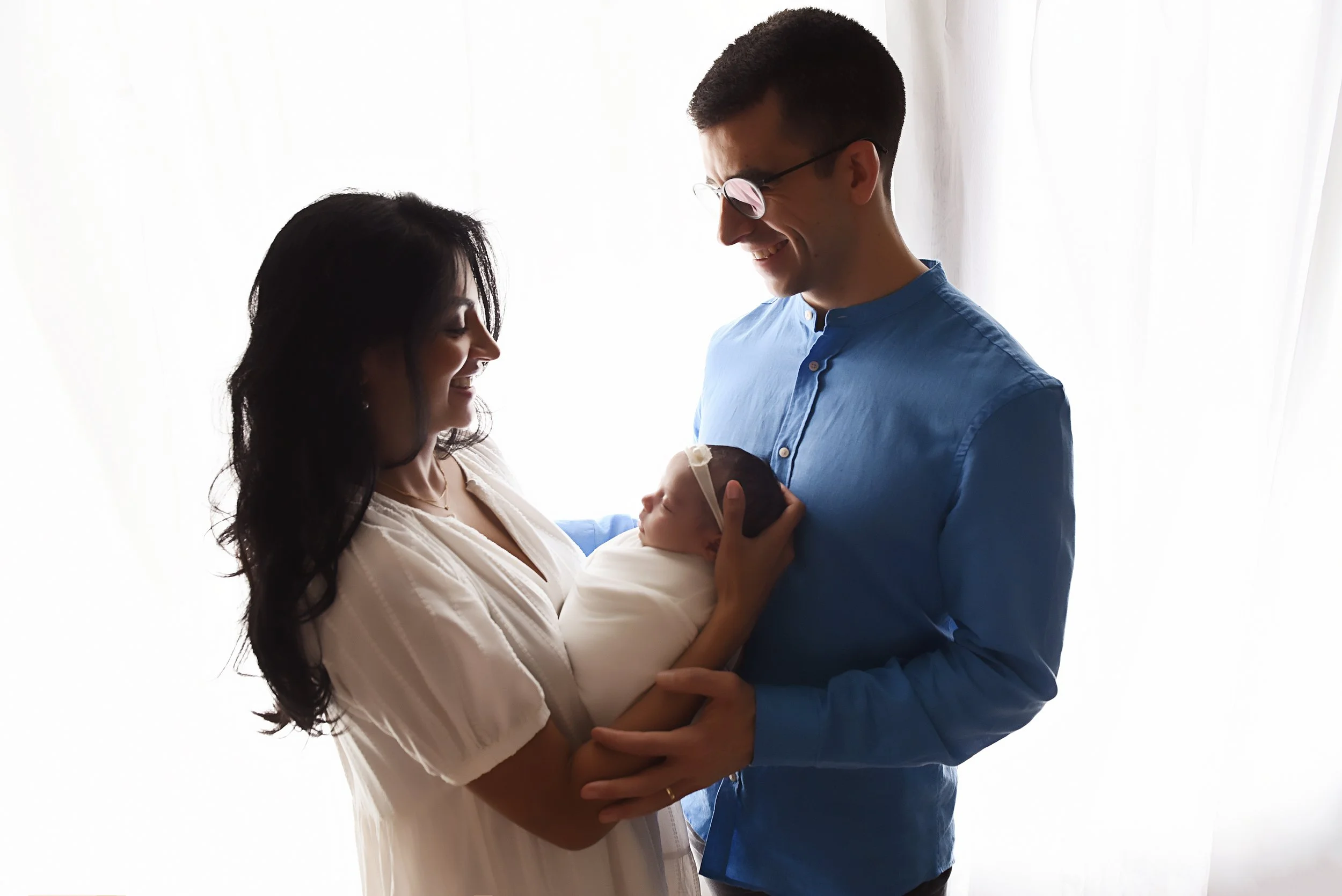 Newborn baby girl cradled by both parents in the studio