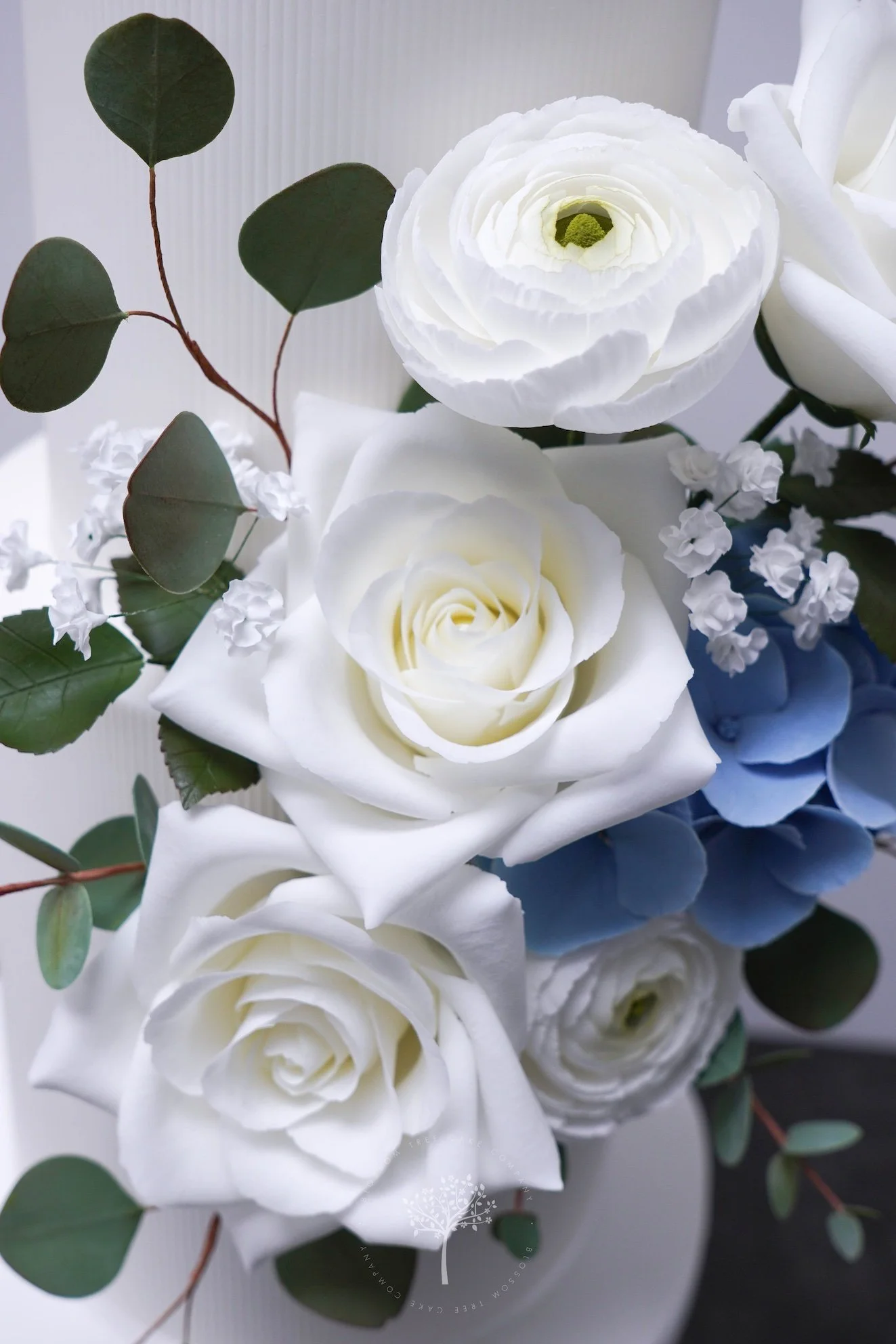 Close‑up of handcrafted sugar roses, ranunculus, hydrangeas, and eucalyptus against a white textured cake, created by Blossom Tree Cake Company for luxury Yorkshire weddings at venues such as Goldsborough Hall.
