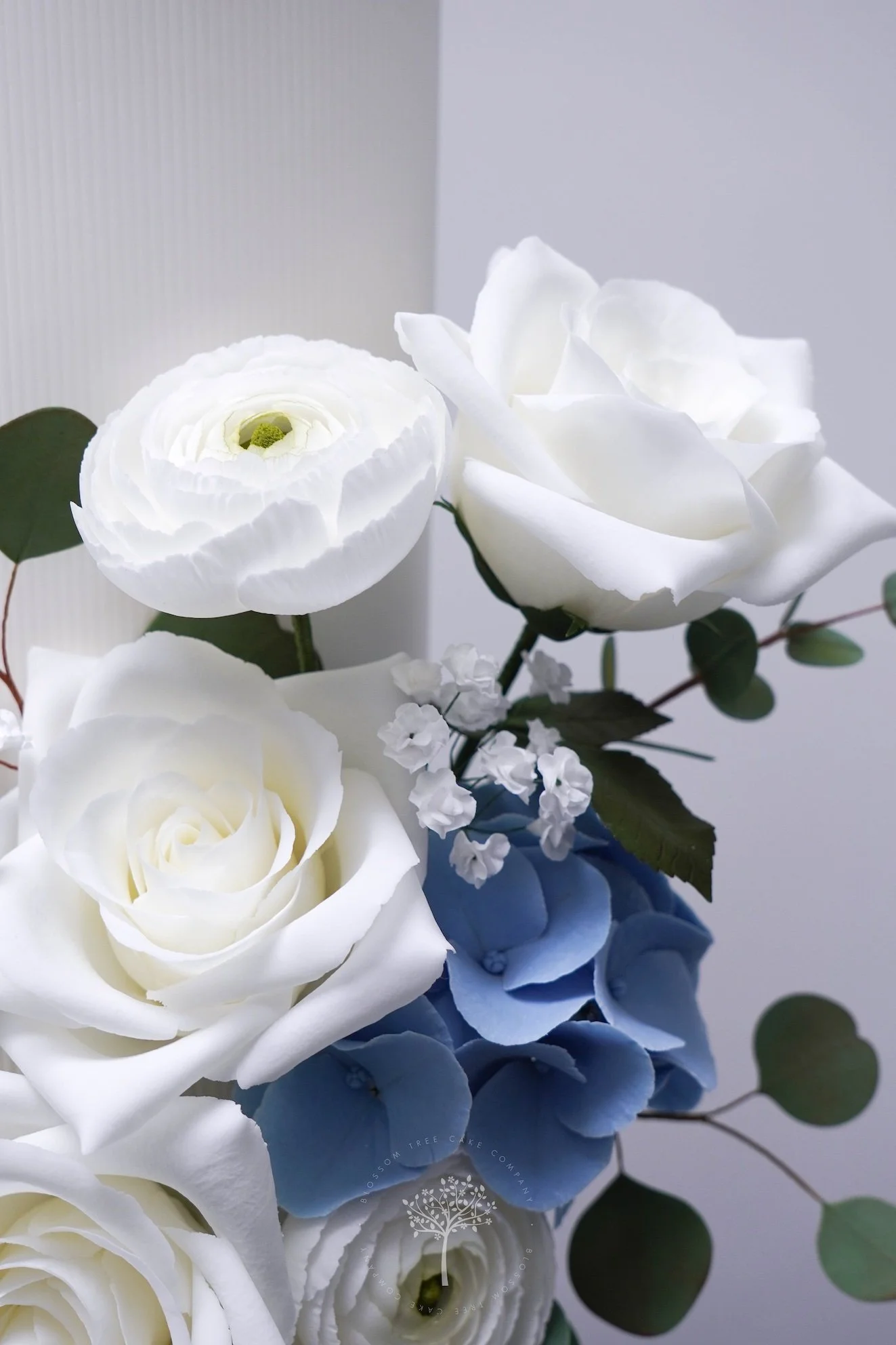 White wedding cake with ribbed texture and handcrafted sugar roses, ranunculus, hydrangeas, and eucalyptus, created by Blossom Tree Cake Company for luxury Yorkshire weddings at venues such as Goldsborough Hall.