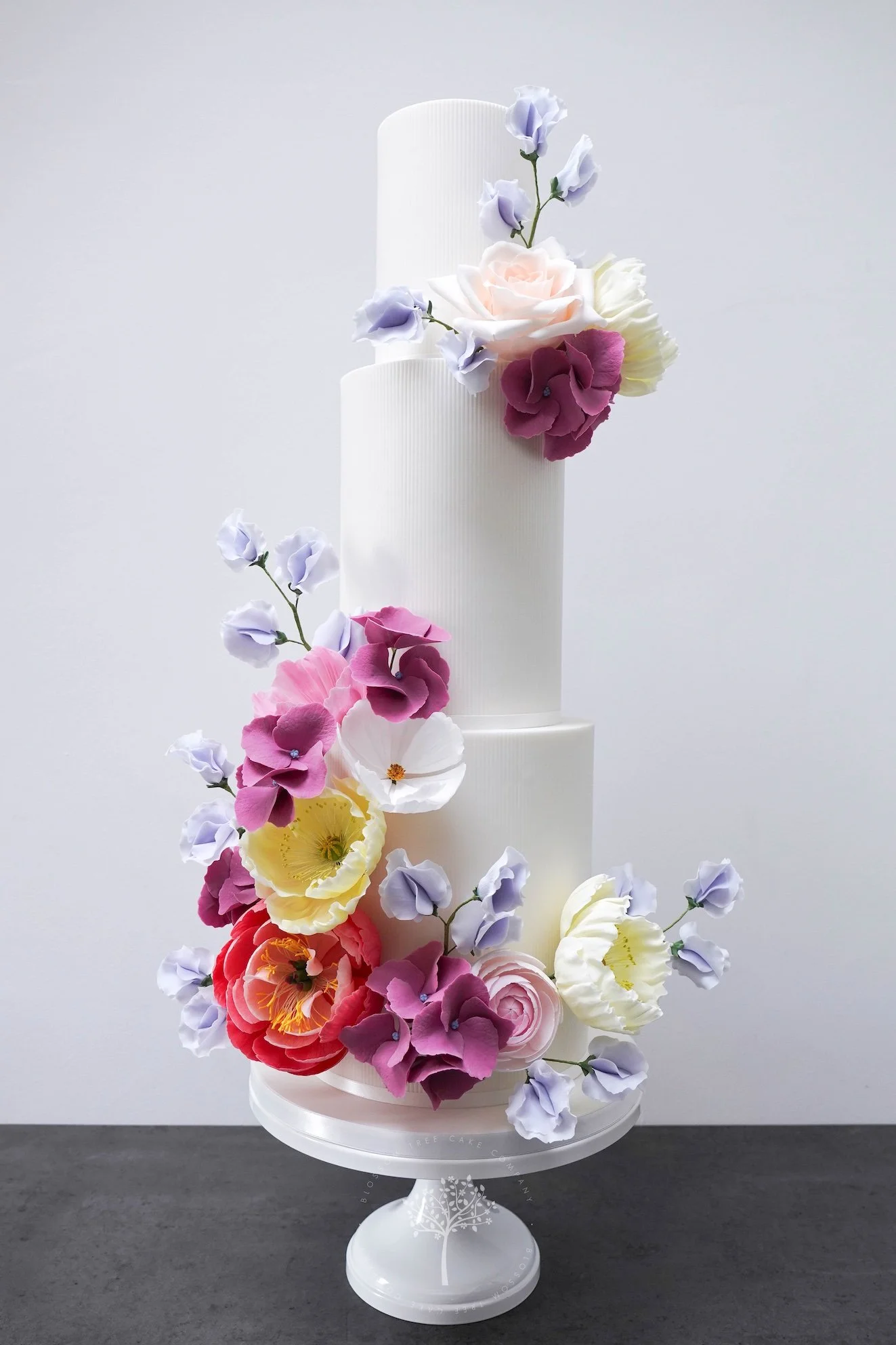 Four‑tier luxury wedding cake by Blossom Tree Cake Company in North Yorkshire, featuring a romantic cascade of handcrafted sugar roses, peonies, and sweet peas in pastel and vibrant tones.