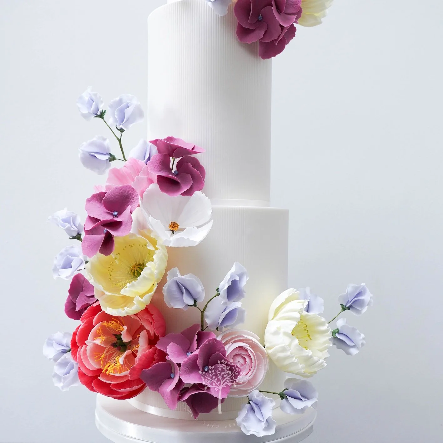 Close‑up of a Blossom Tree Cake Company wedding cake with delicate handcrafted sugar flowers, including white and pink blooms with lilac and magenta accents, arranged on a softly textured white tier for an elegant, romantic finish.