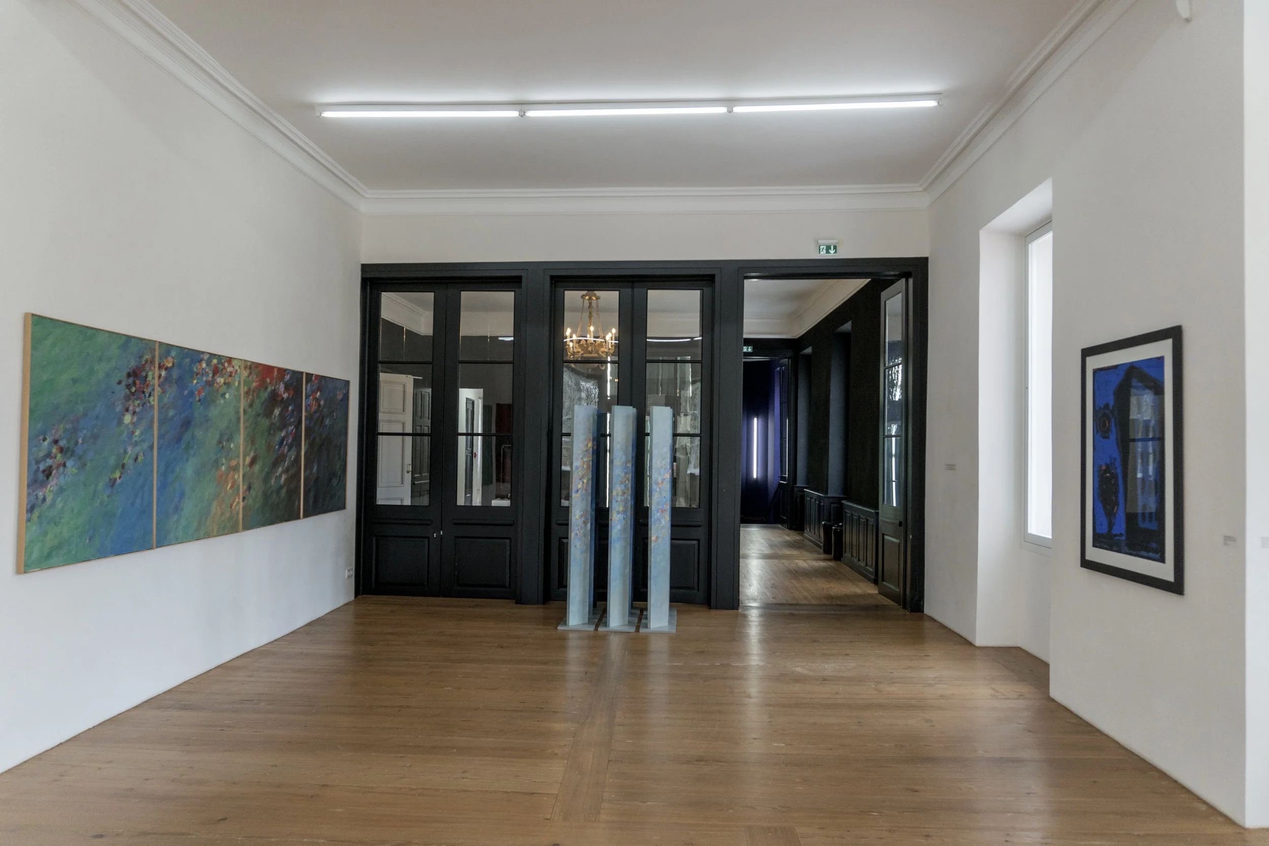 Boiseries noires et plancher de bois blond où faire glisser des souliers de bal, sous un lustre ancien en bronze doré... en contre-point de la sérénité fluide et colorée de deux oeuvres récentes d' Emil Kiess.