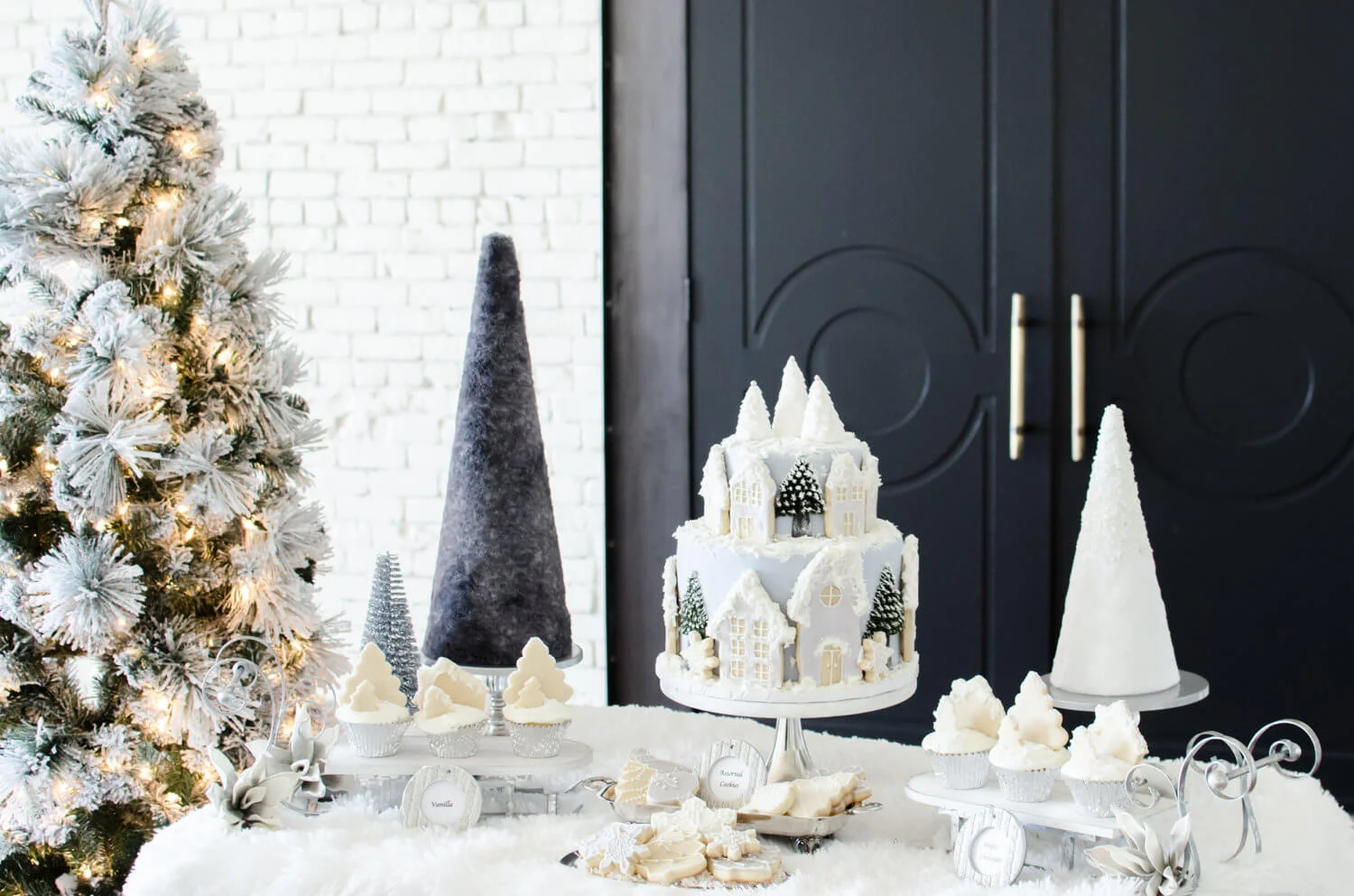 Christmas-style winter bridal shower dessert table with a flocked tree, white village cake, tree-shaped cookies and cupcakes