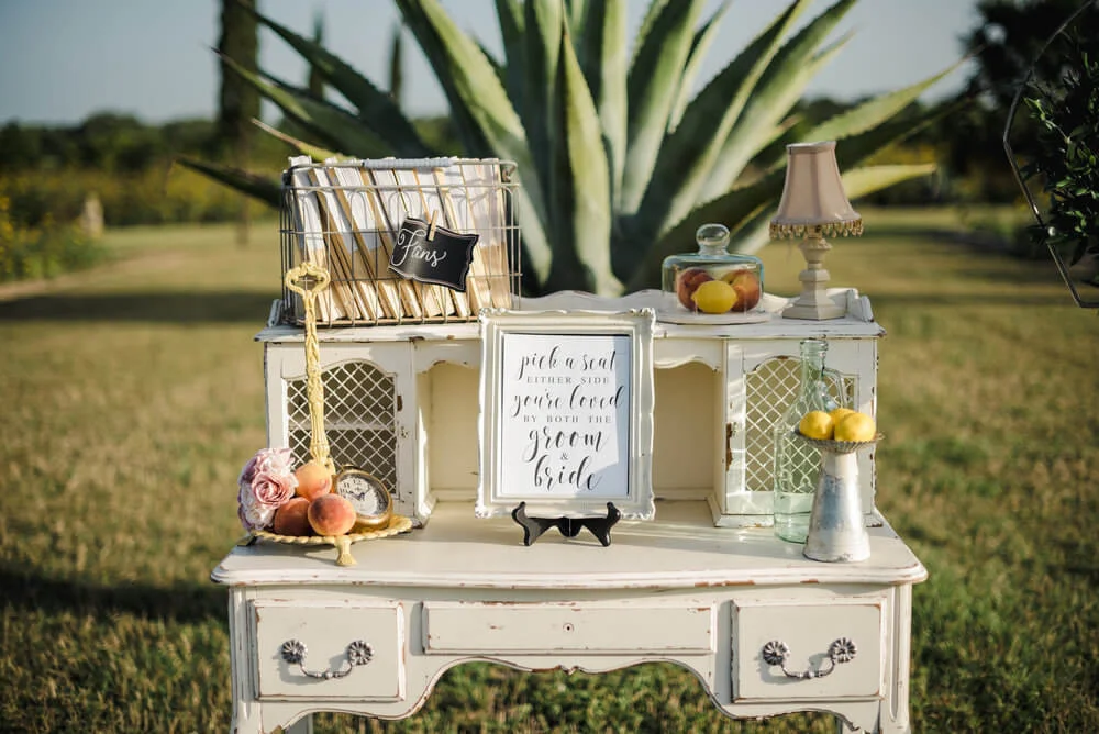French country wedding inspiration vintage desk with antique suitcases, fans, ceremony programs, lemons, and peaches, with decor.