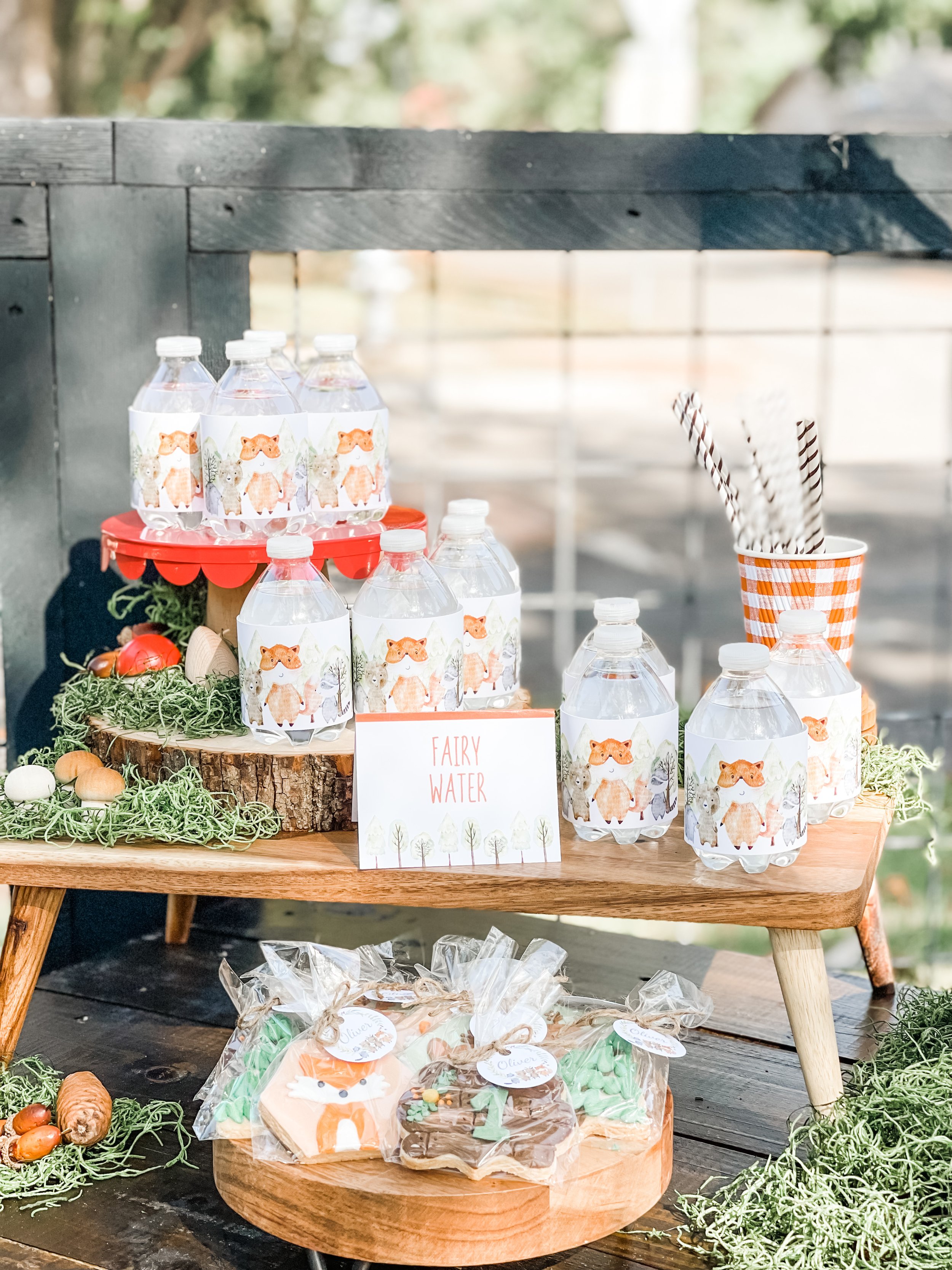  Woodland forest party drink station with animal and plant decorations and water bottles wrapped in woodland creature labels set up on wooden stands. 