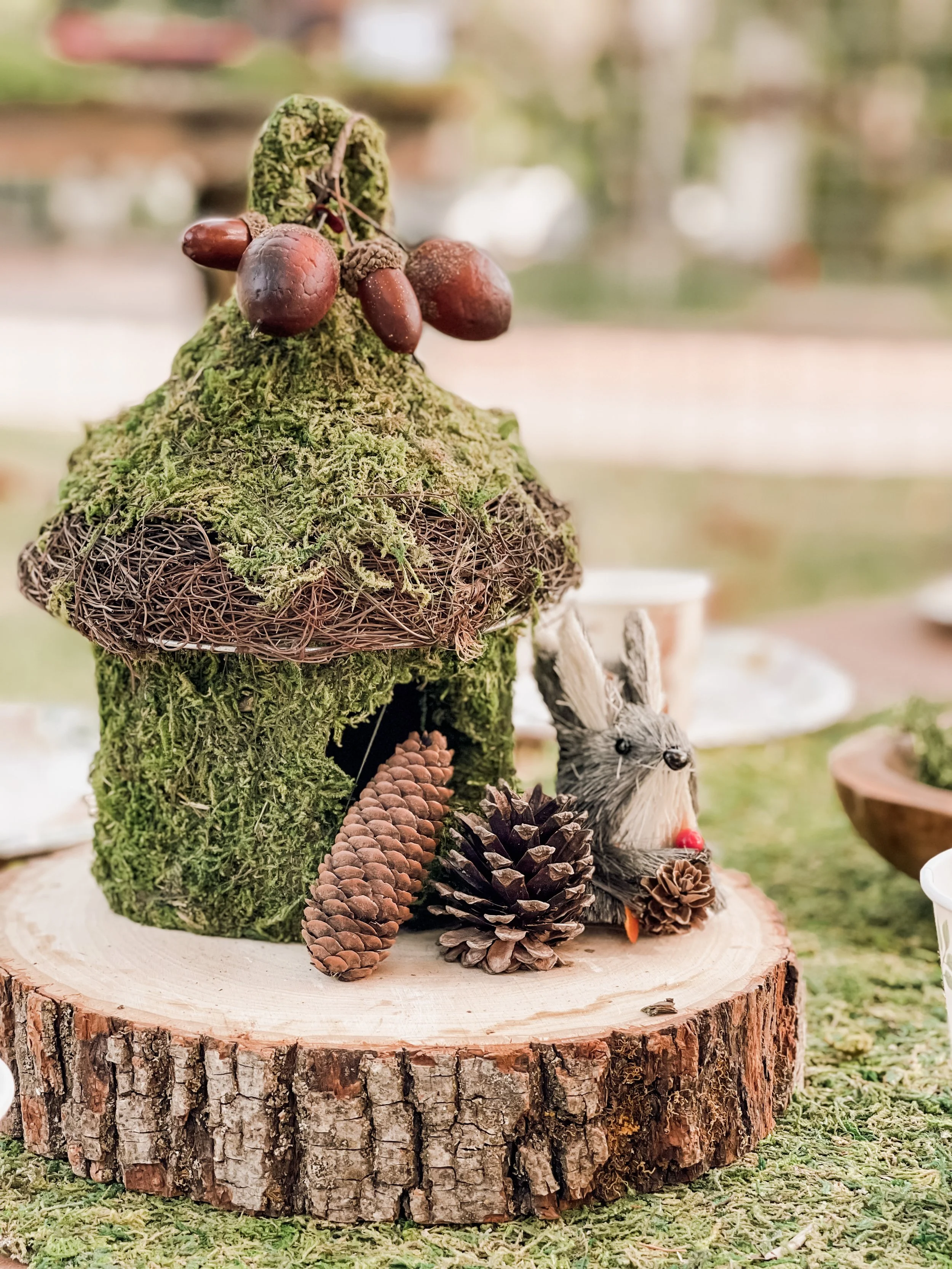  outdoor woodland party centerpiece with mossy house, pinecones, and woodland animal decorations 